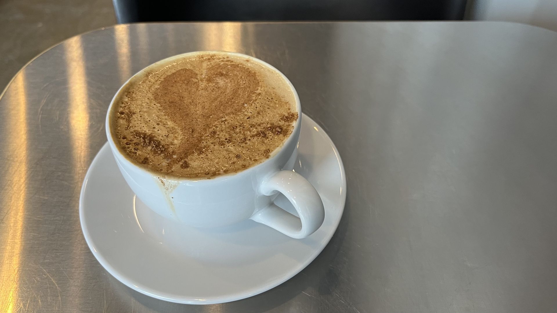 A latte on a plate on a silver table