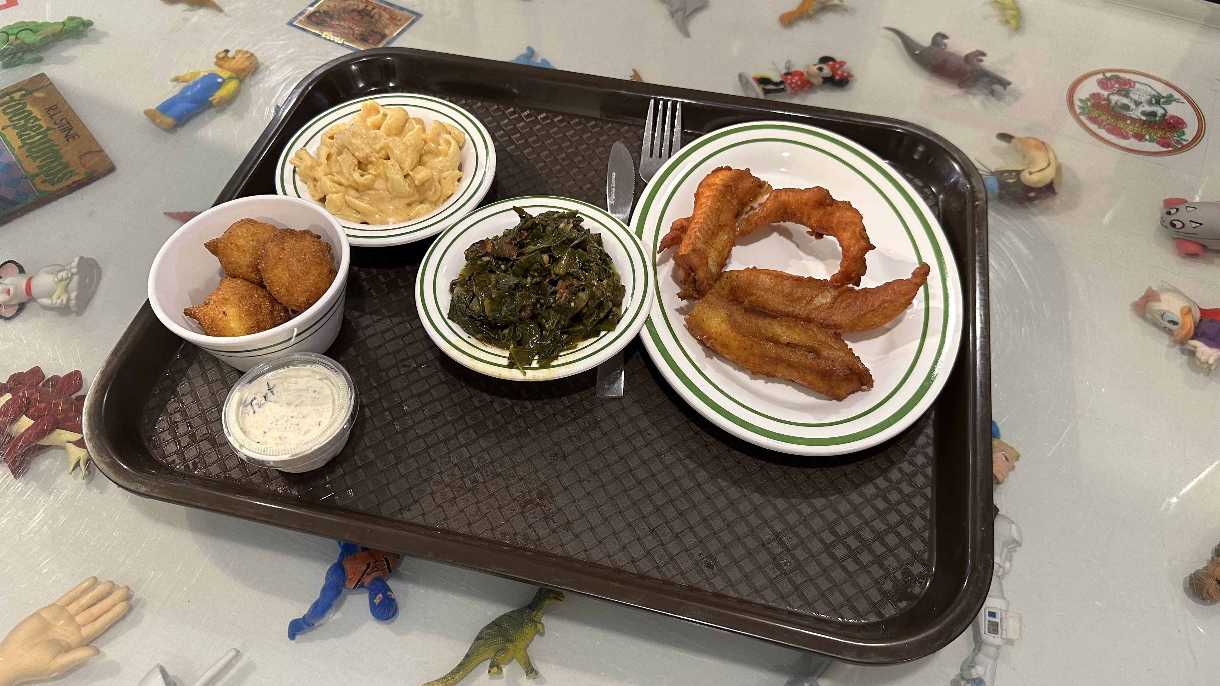 A cafeteria tray filled with fried catfish, collard greens, macaroni and cheese and hush puppies.
