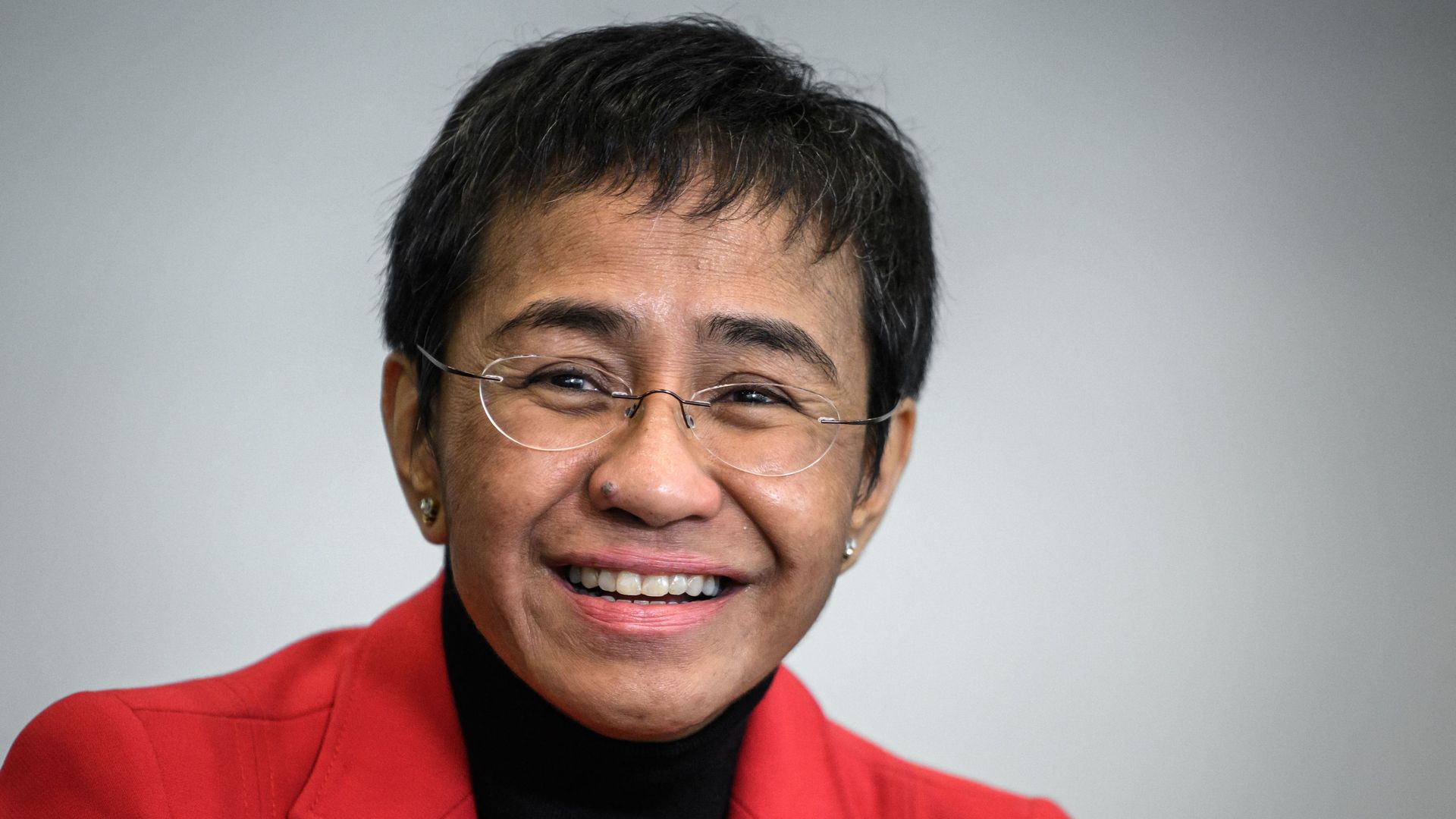 Photo of Maria Ressa smiling wearing glasses and a red jacket