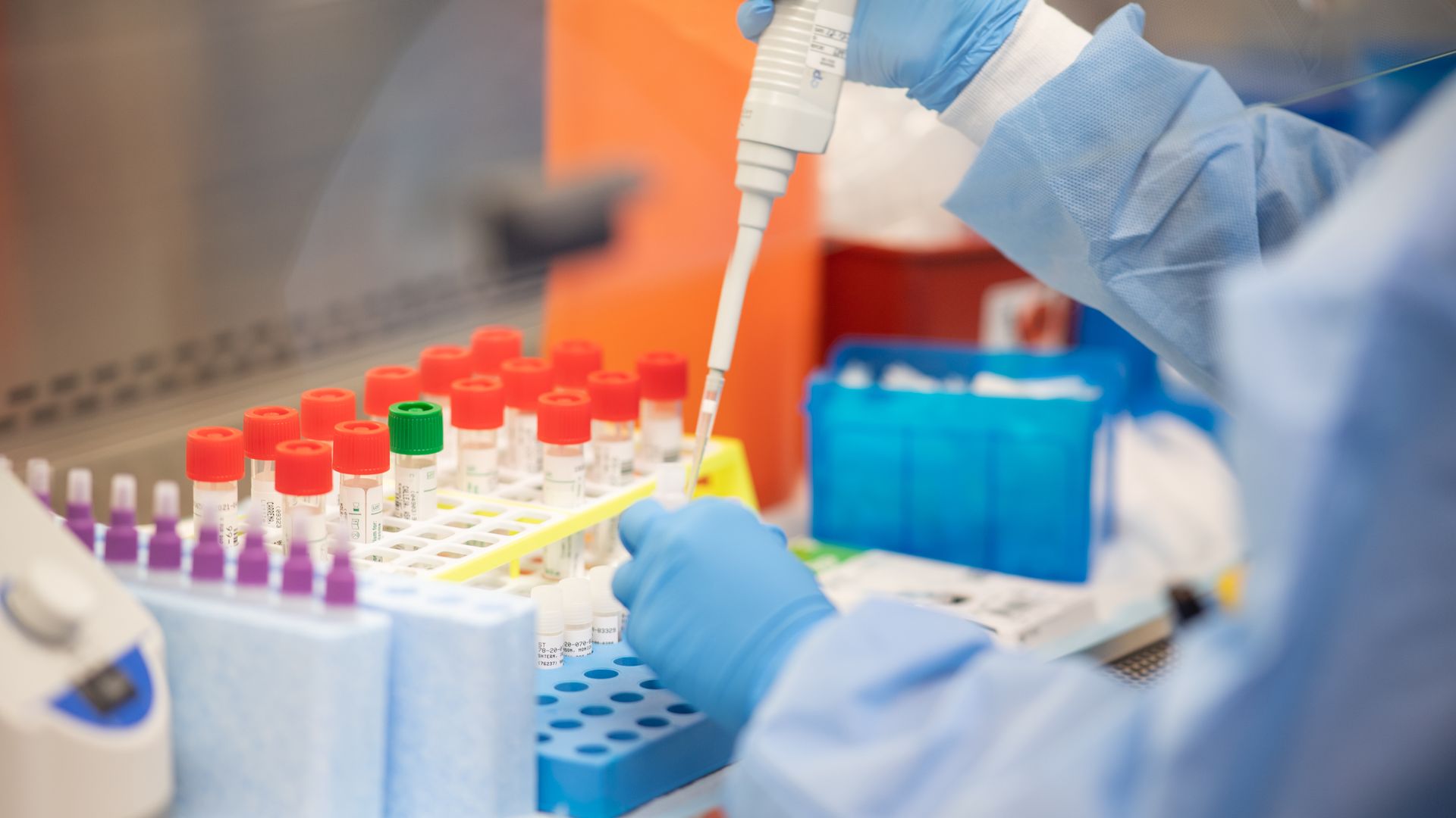 A lab technician with blue gloves handles test tubs for coronavirus tests.