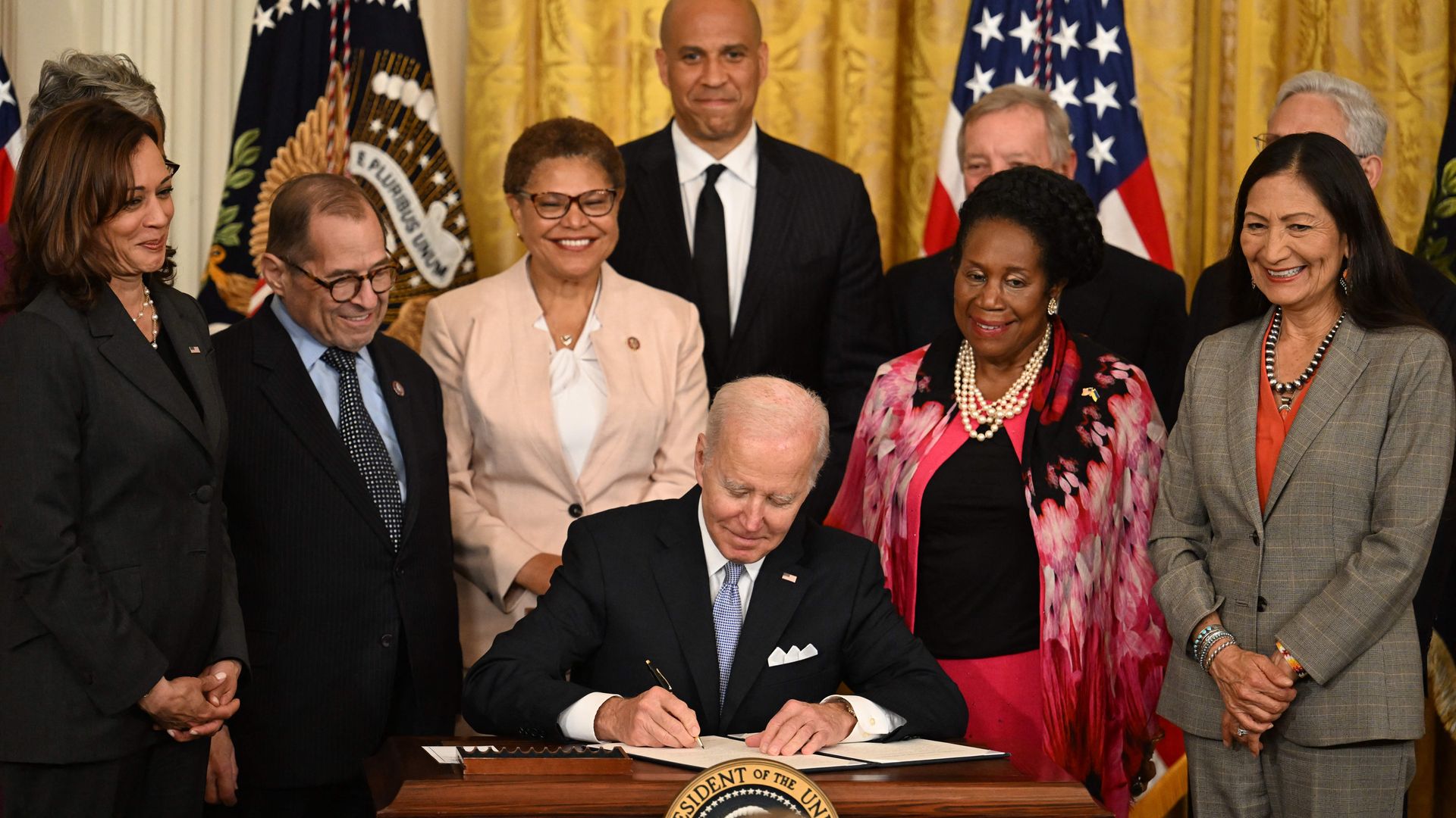 Photo of Joe Biden signing a bill at a desk while people stand around him smiling