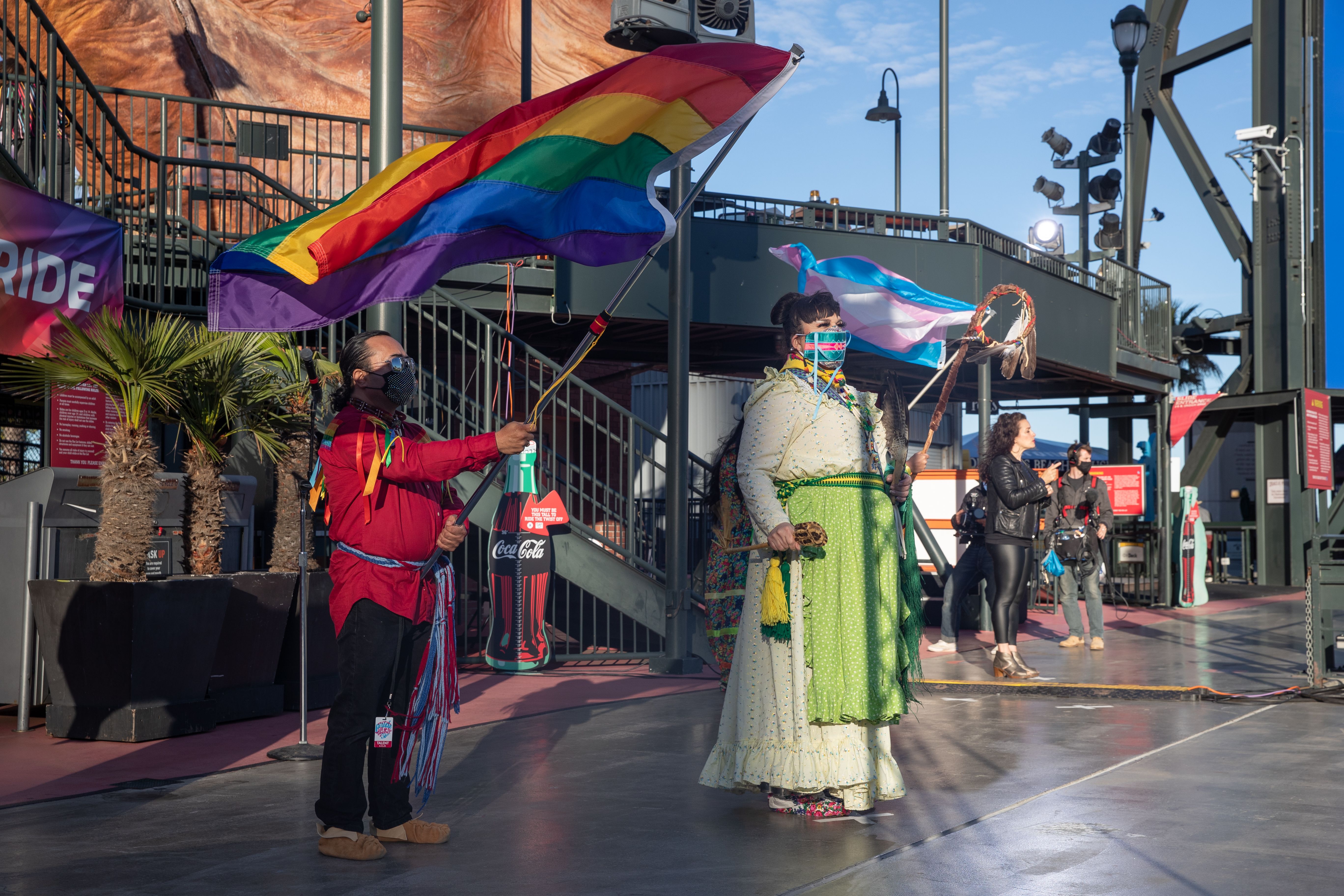 Photo of two Native people waving a rainbow flag on the stage