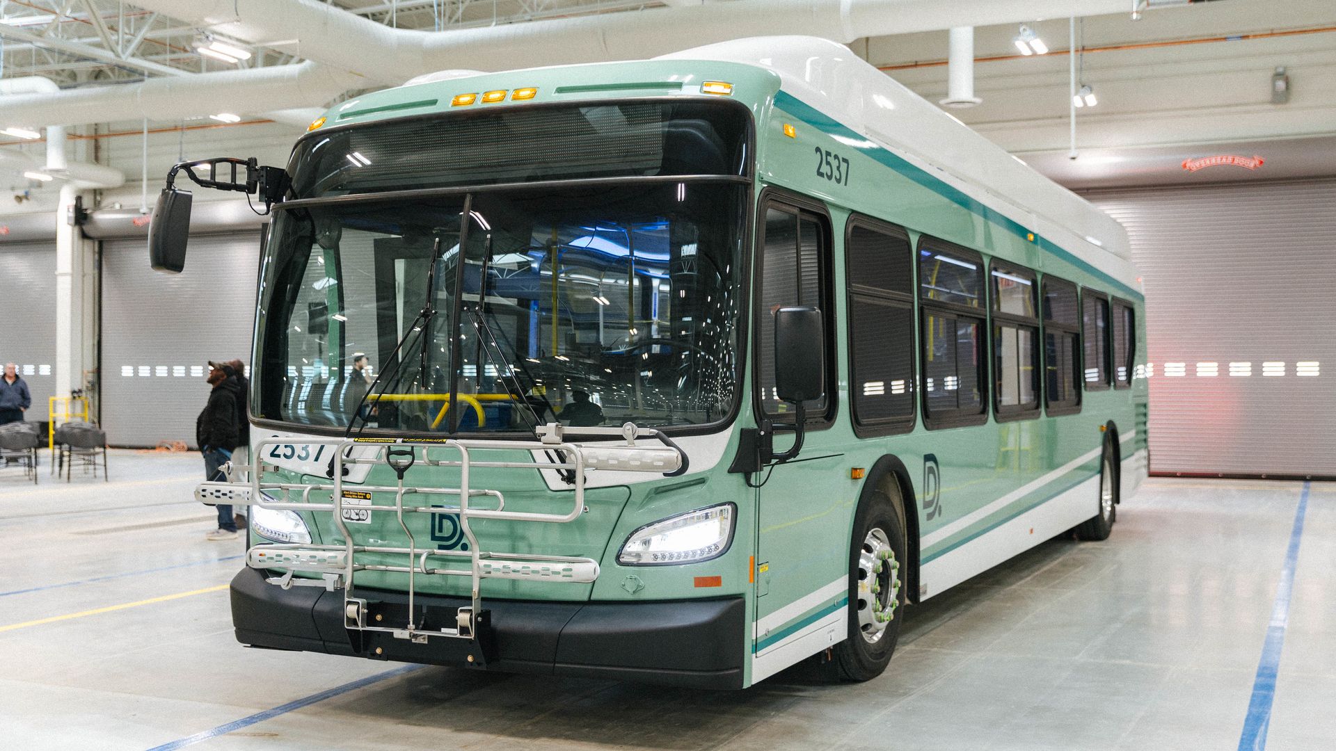 A new, green bus sits parked in a warehouse