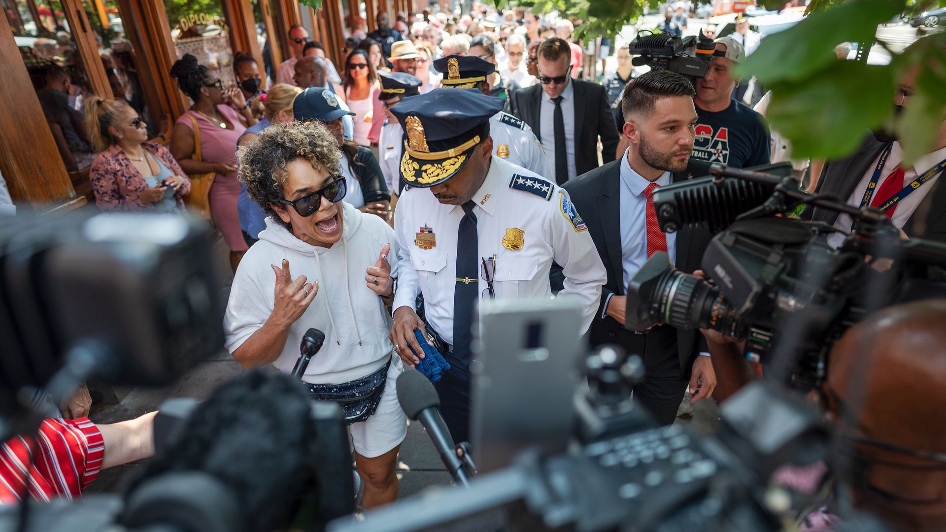 Police Chief Robert Contee in the center is surrounded by residents, officials, and TV cameras at a public event in response to crime