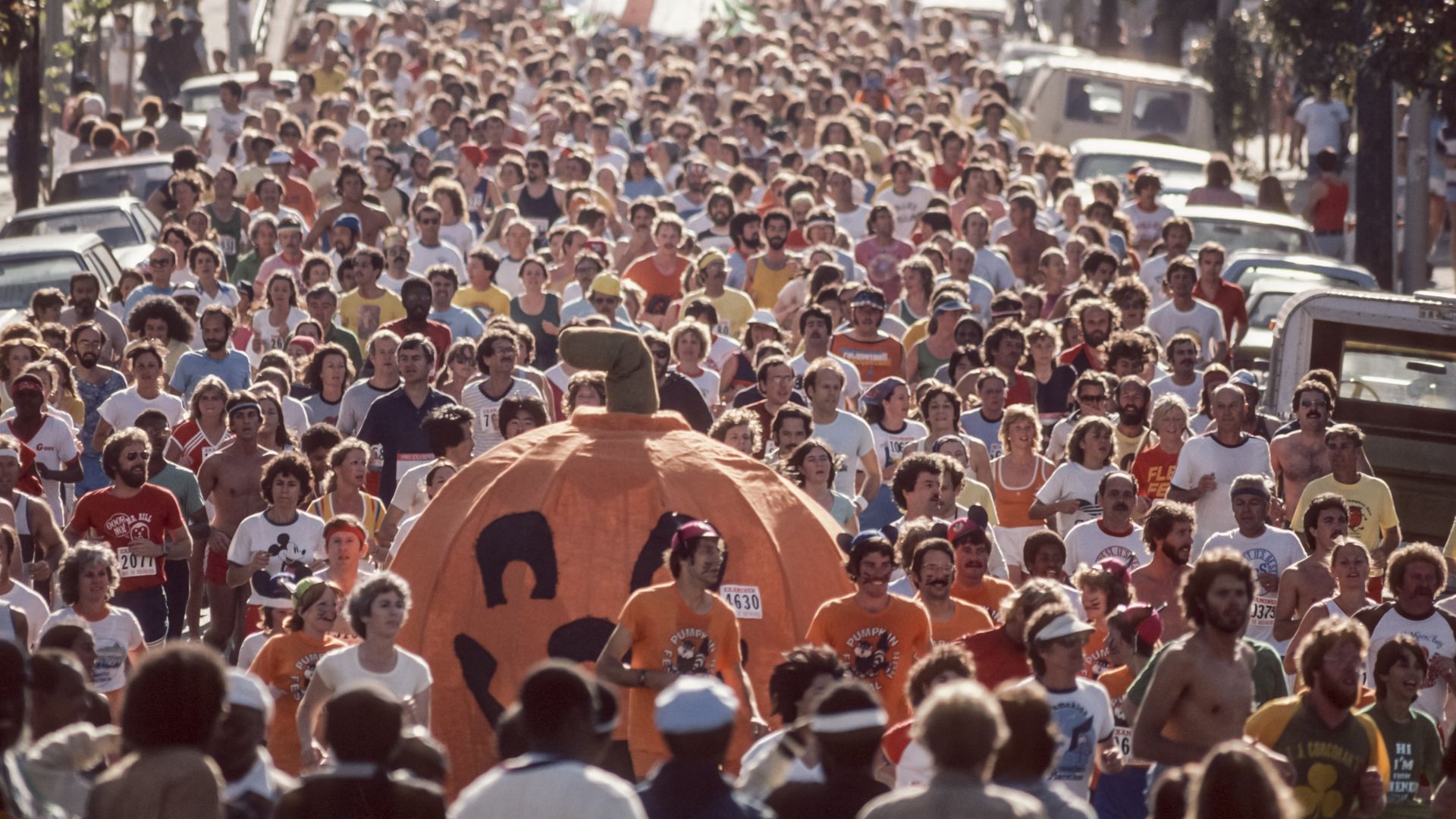 Photo of tons of people running in the street with a giant jack-o-lantern pumpkin in the middle