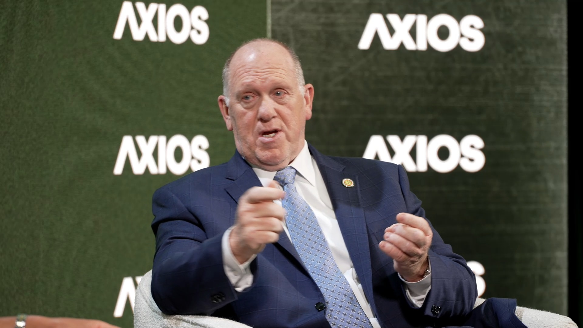 Tom Homan in a navy blue suit and light blue patterned tie speaking. 