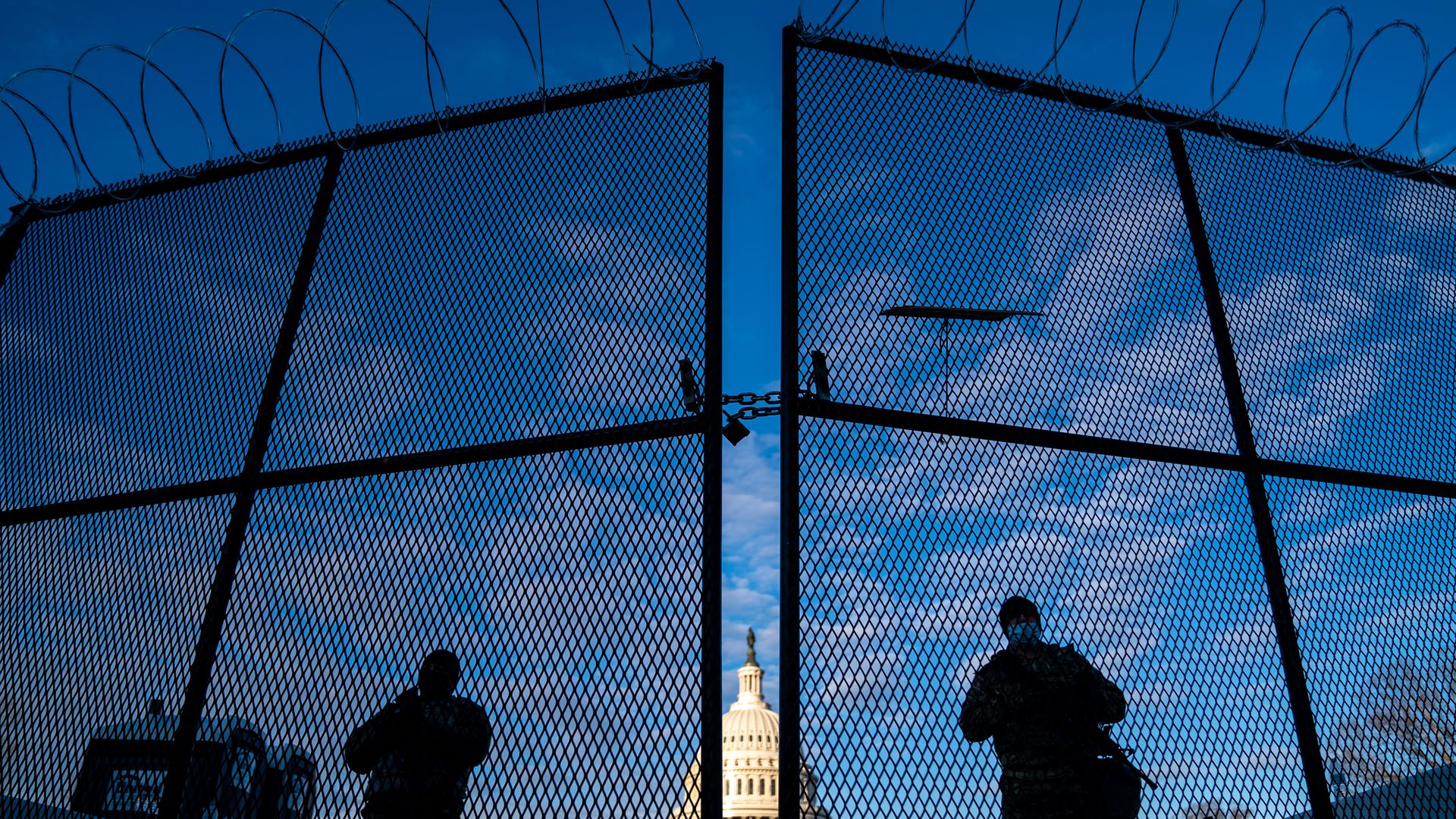 National Guardsmen and a tall fence are seen protecting the U.S. Capitol in the background.