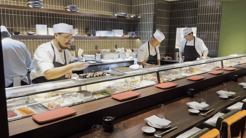 Three chefs prepare sushi in an open kitchen.