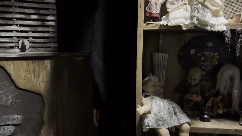 A gif of a scary clown girl peeking out from behind a bookcase filled with creepy dolls