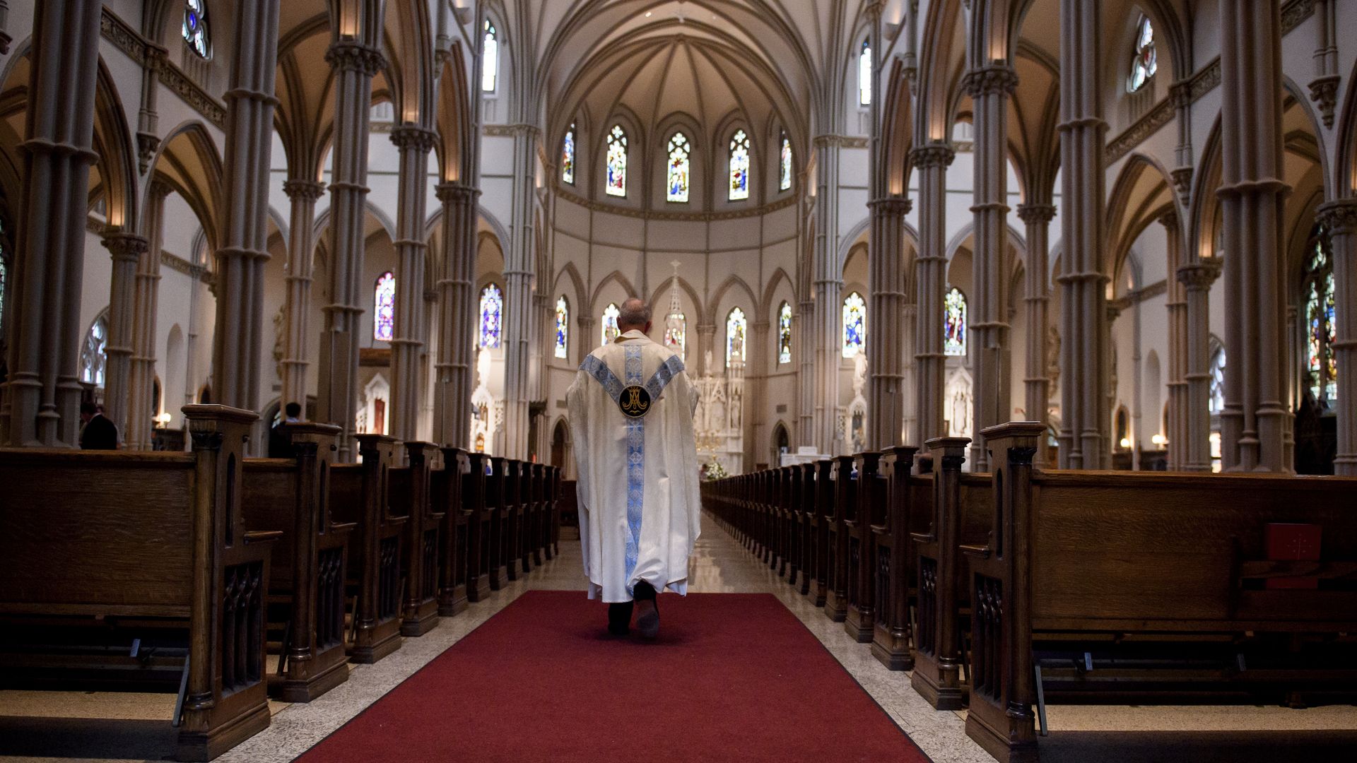 A priest walks down the corridors of church pews.