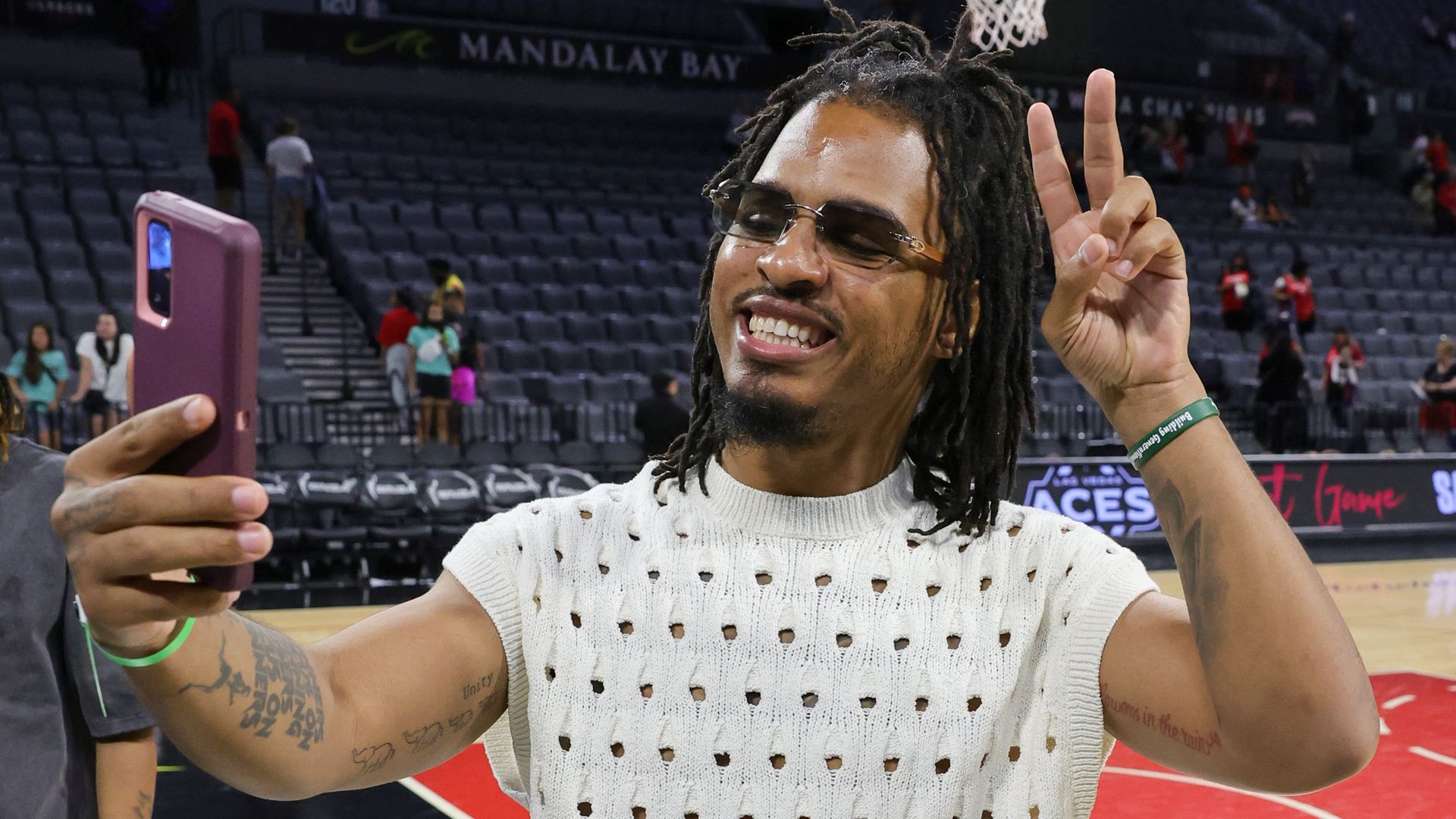Keith Lee stands on an empty basketball court and films a selfie with one hand while smiling and holding up a peace sign with his other hand.