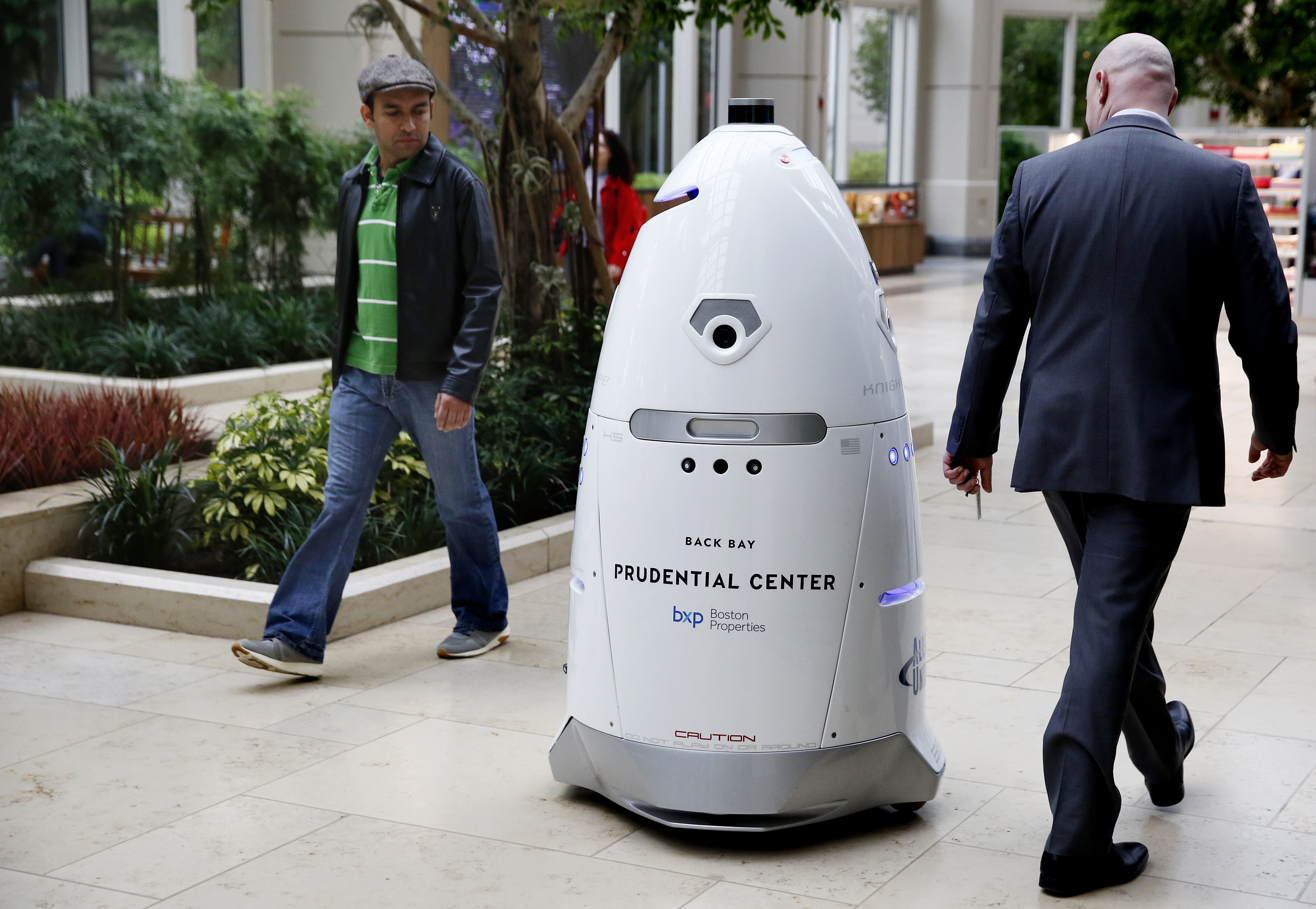 Les piétons vérifient le garde de sécurité robotique alors qu'il se promène dans le centre commercial.