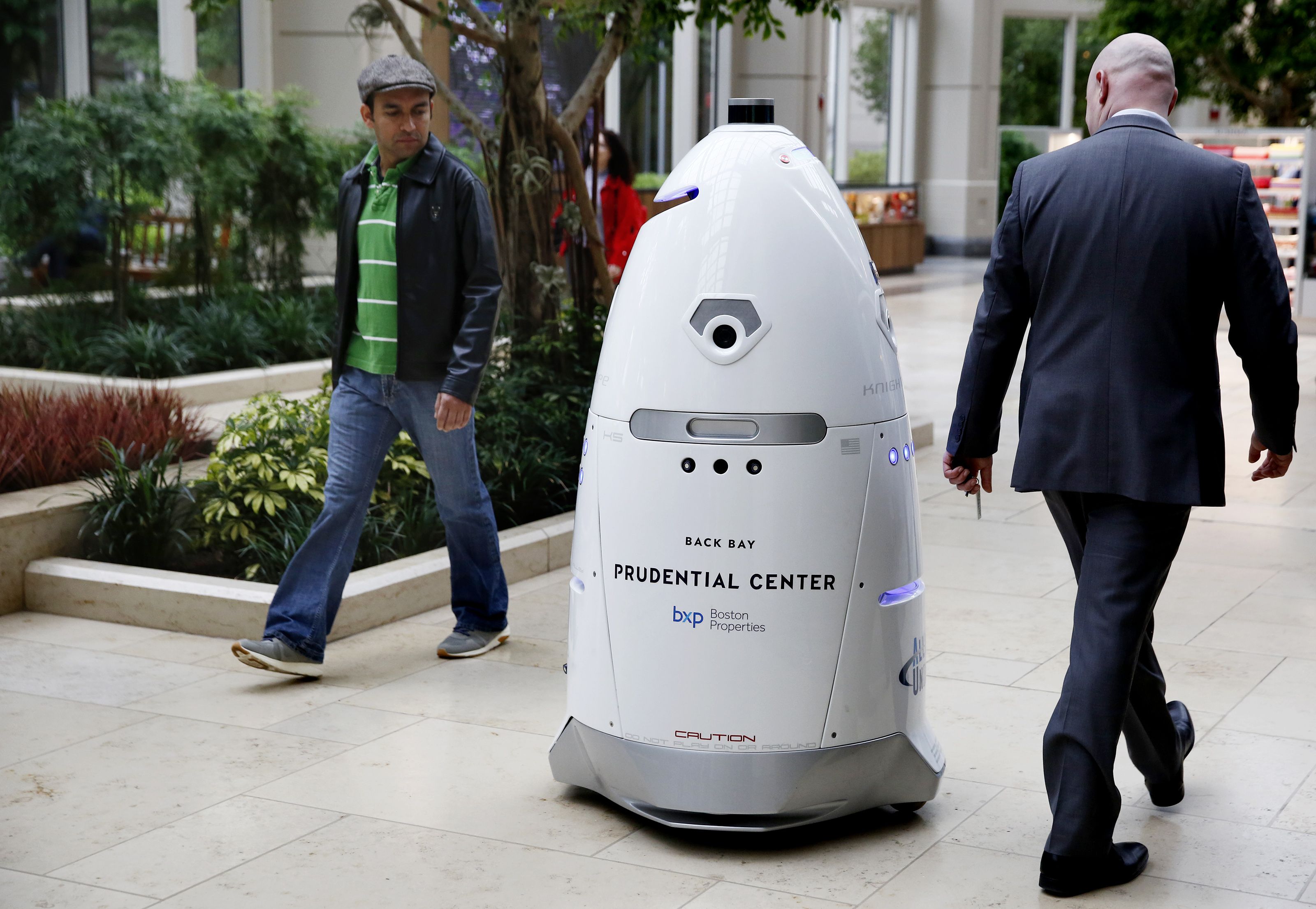 Pedestrians eyeball a robot security guard as it strolls by in a shopping plaza.