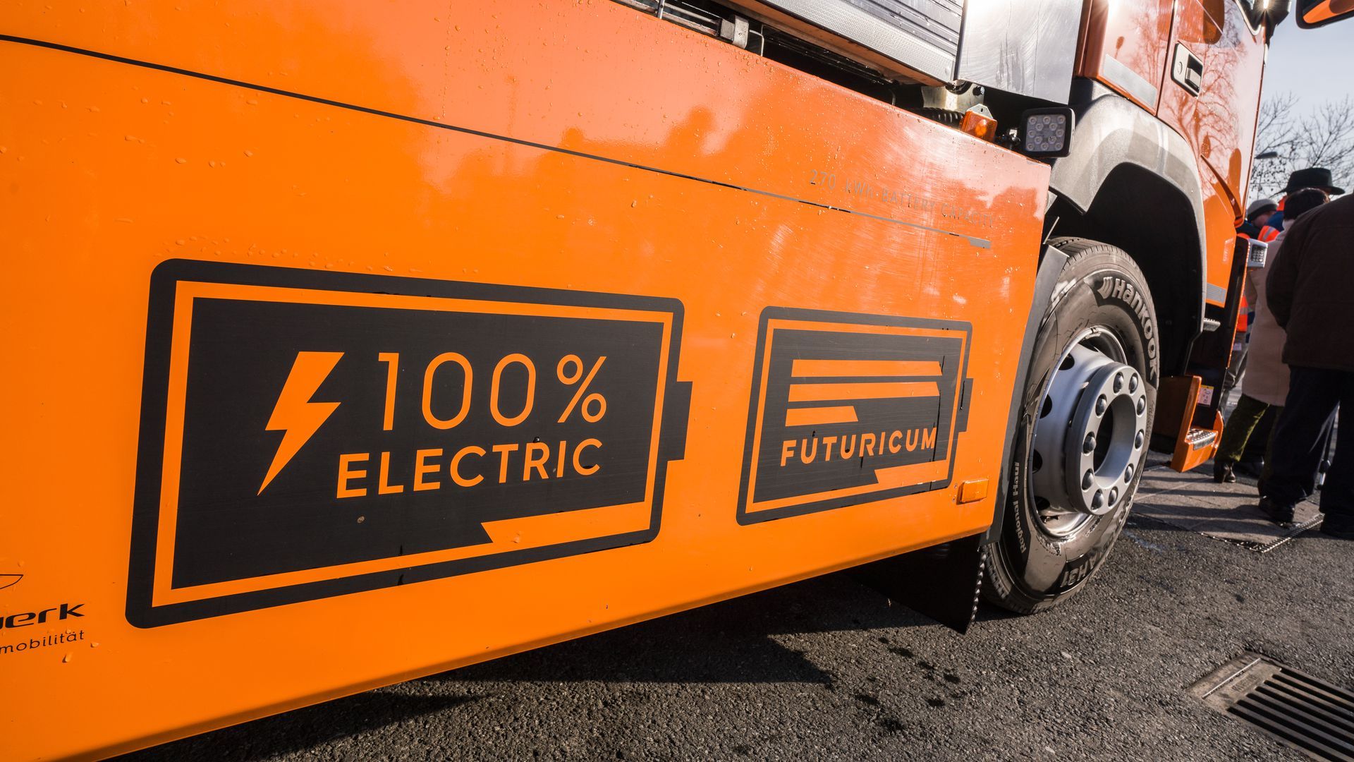 A photo of the side of an orange electric trash truck that says "100% electric."