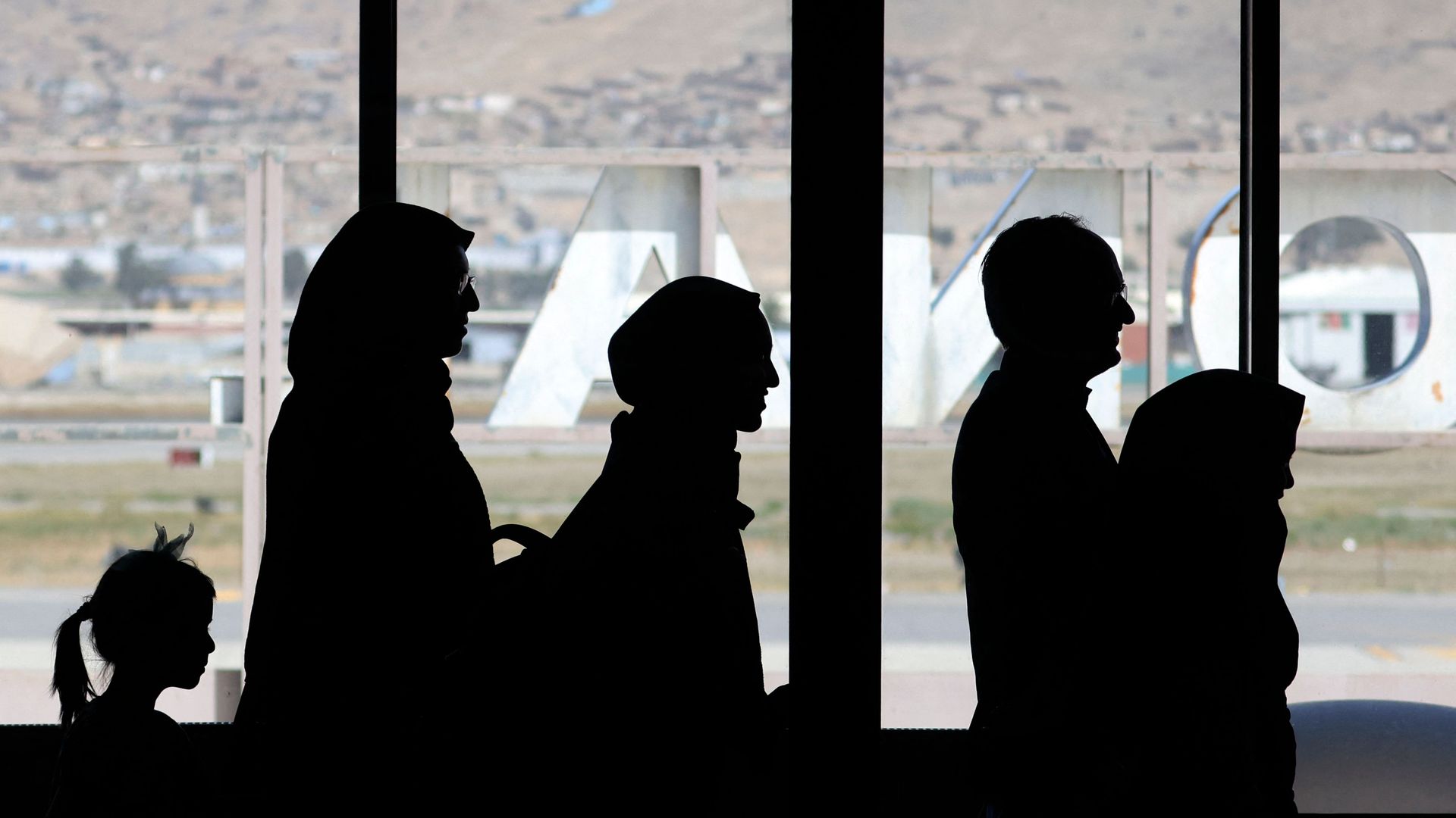 Photo of silhouettes of five people waiting in line inside an airport terminal