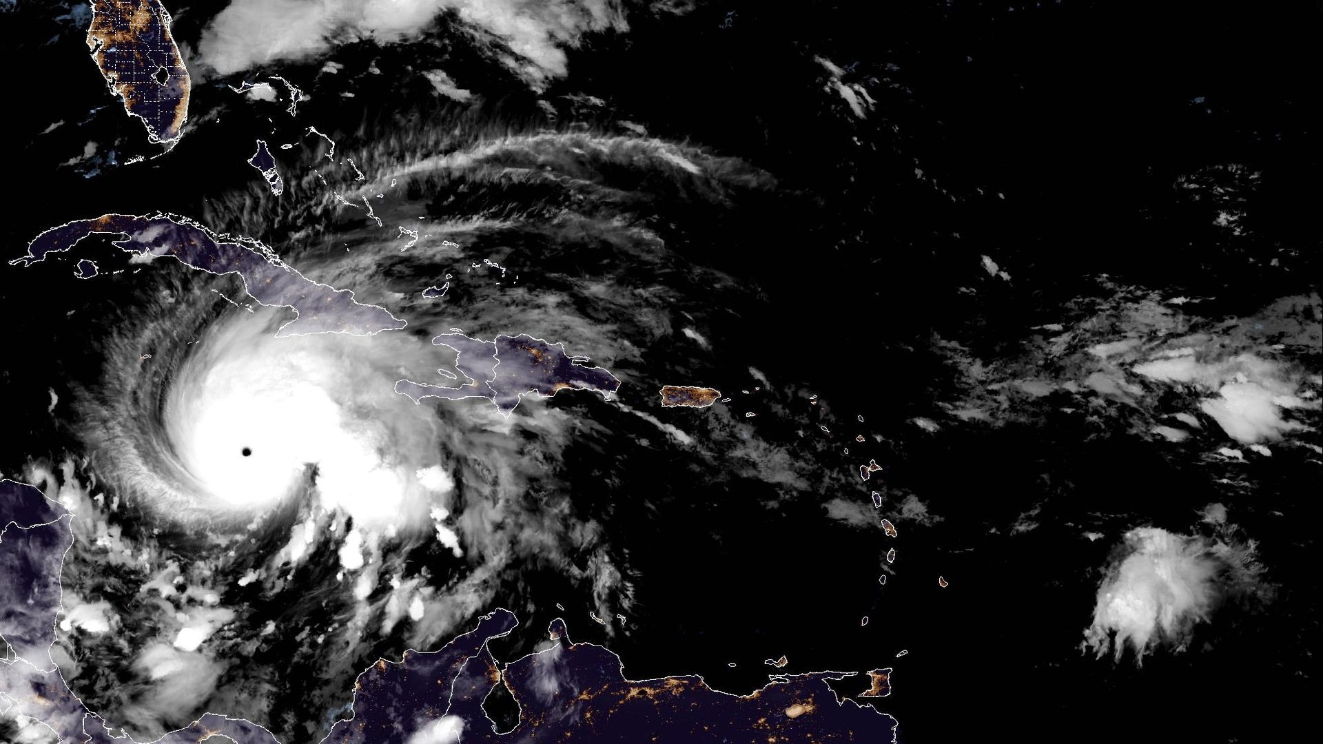 Satellite image showing a large hurricane with a distinct eye near Cuba in the Caribbean against a nighttime backdrop, with visible cloud formations and coastlines.