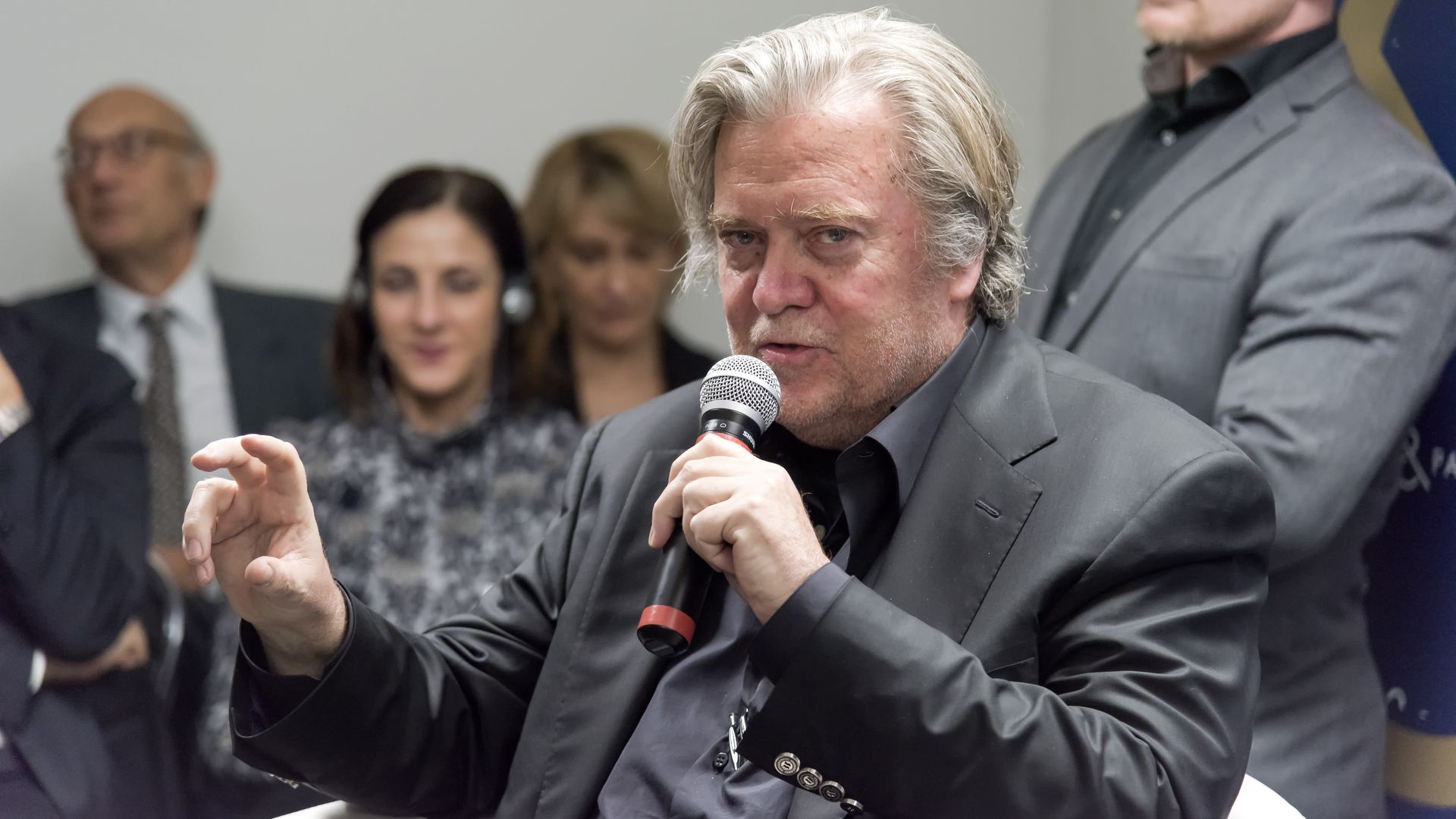 In this image, Steve Bannon is speaking into a microphone with a crowd behind him. 
