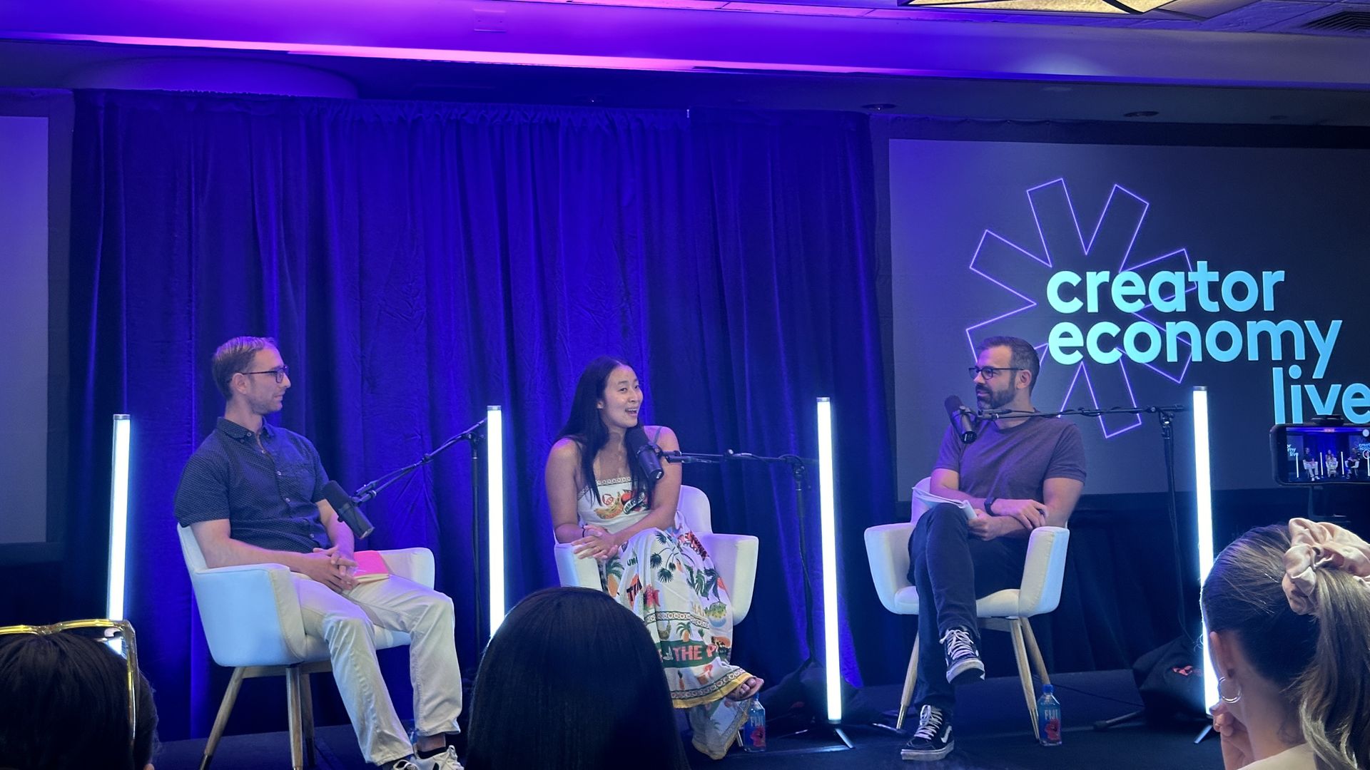 Linqia's Keith Bendes, Creator Authority's Brendan Gahan and August's Nadya Okamoto sitting in white chairs behind podcast microphones by a screen that says Creator Economy Live