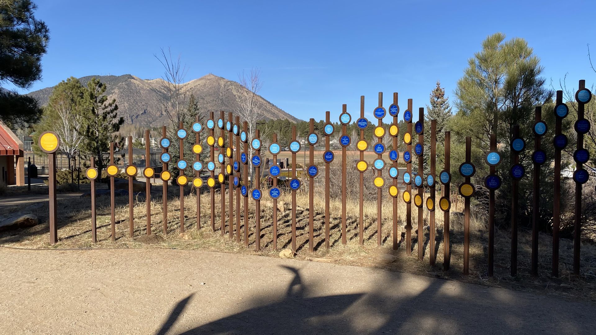 A series of copper-colored poles of varying heights adorned with circles that are yellow, light blue and dark blue.