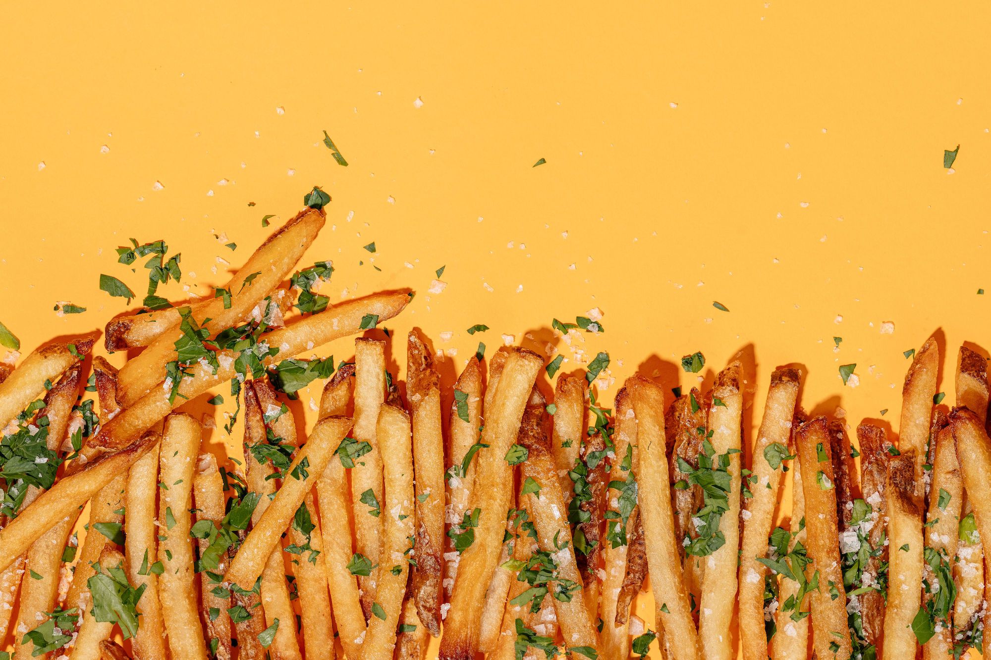 Fries at Jesse & Ben's on a yellow background, dusted with parsley and salt