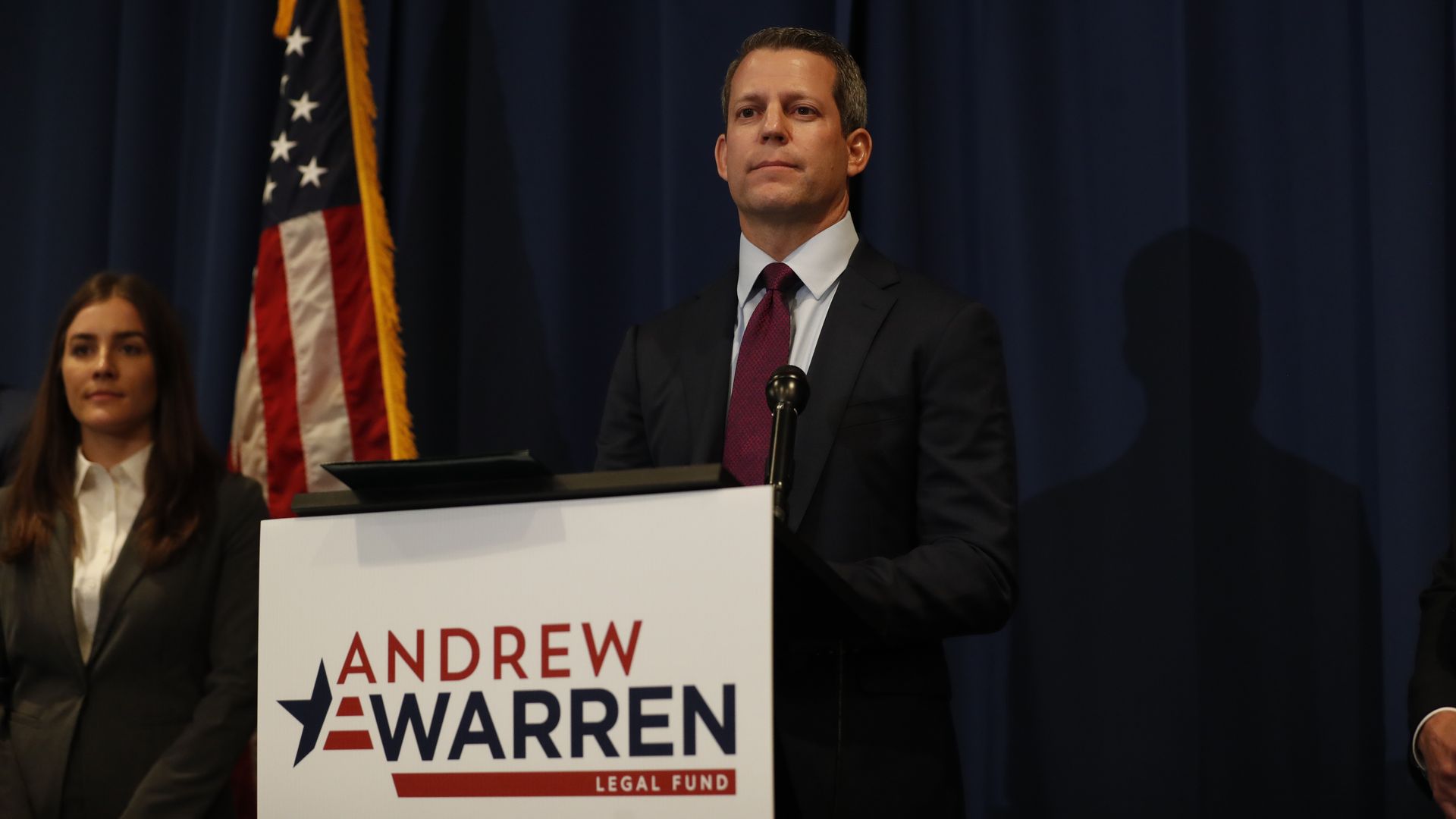 Andrew Warren stands at a podium with a sign reading "Andrew Warren legal fund"