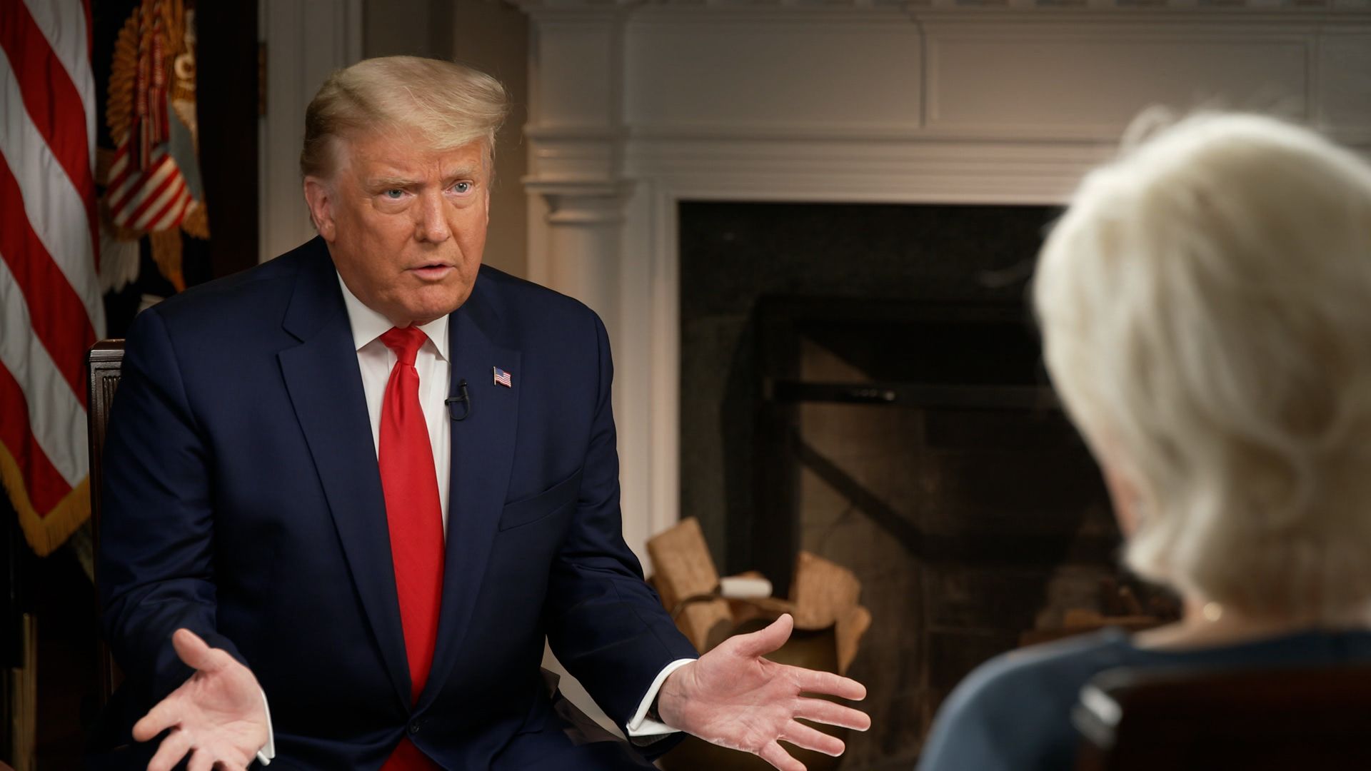Trump wearing a blue suit jacket, white shirt and red tie in front of an interviewer 