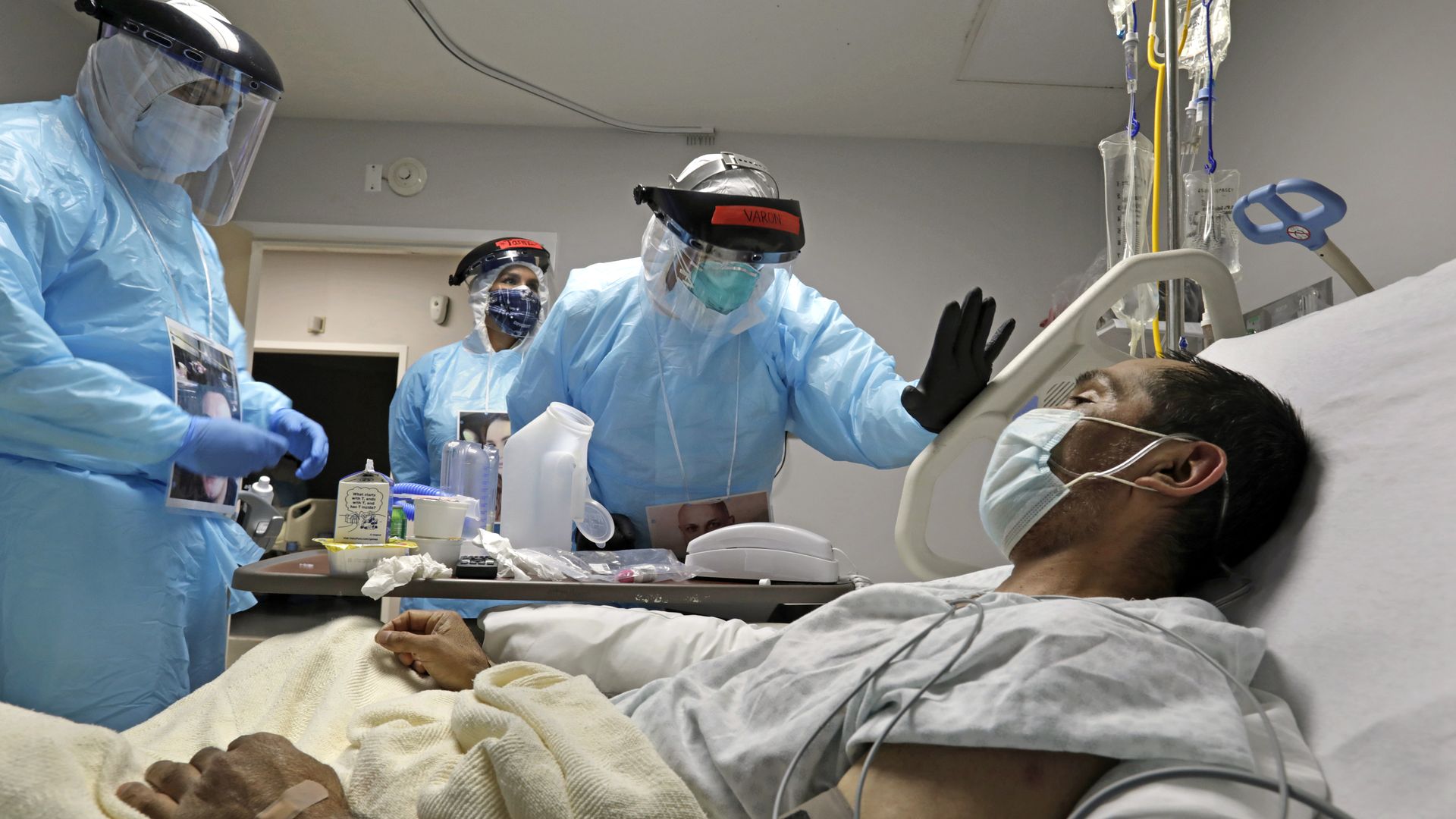 A man lays in bed while masked medical workers stand above him