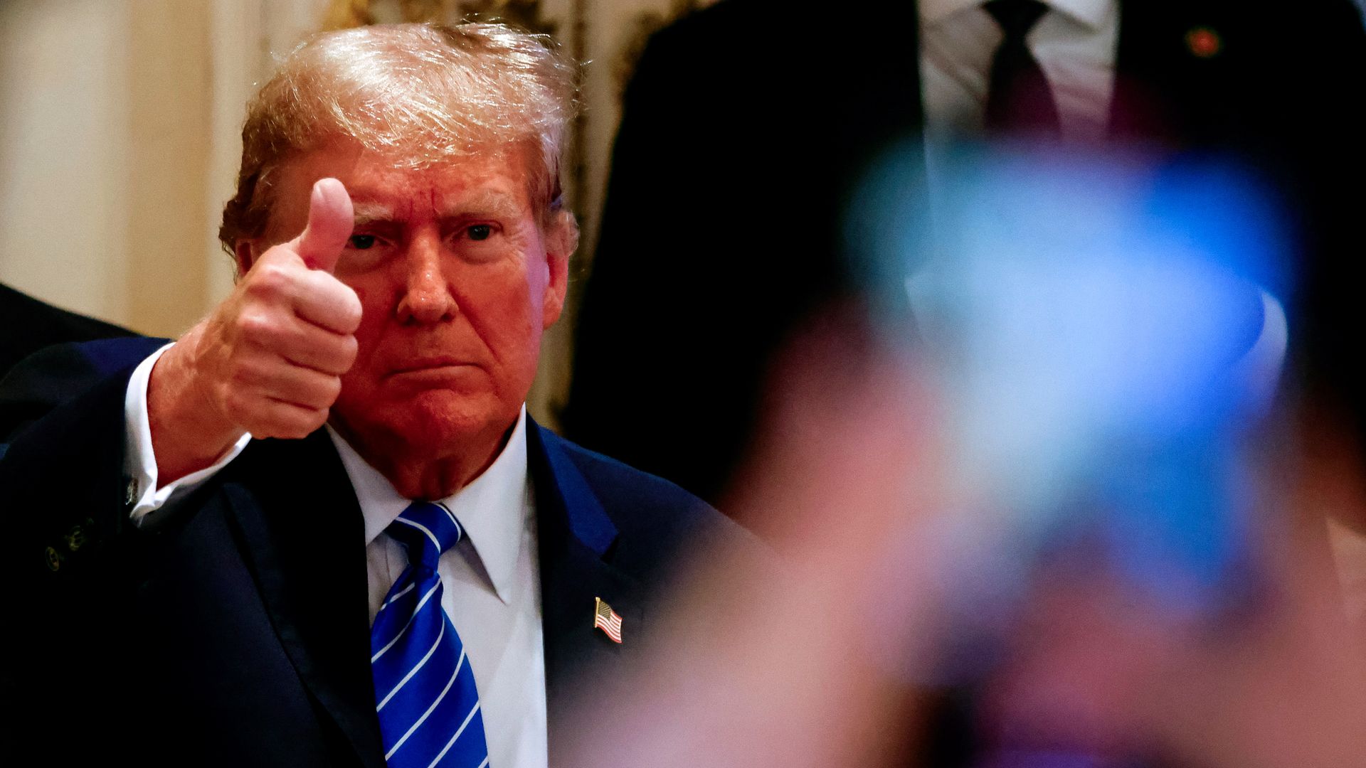 Donald Trump, wearing a blue suit white shirt and blue tie, give a thumbs-up.