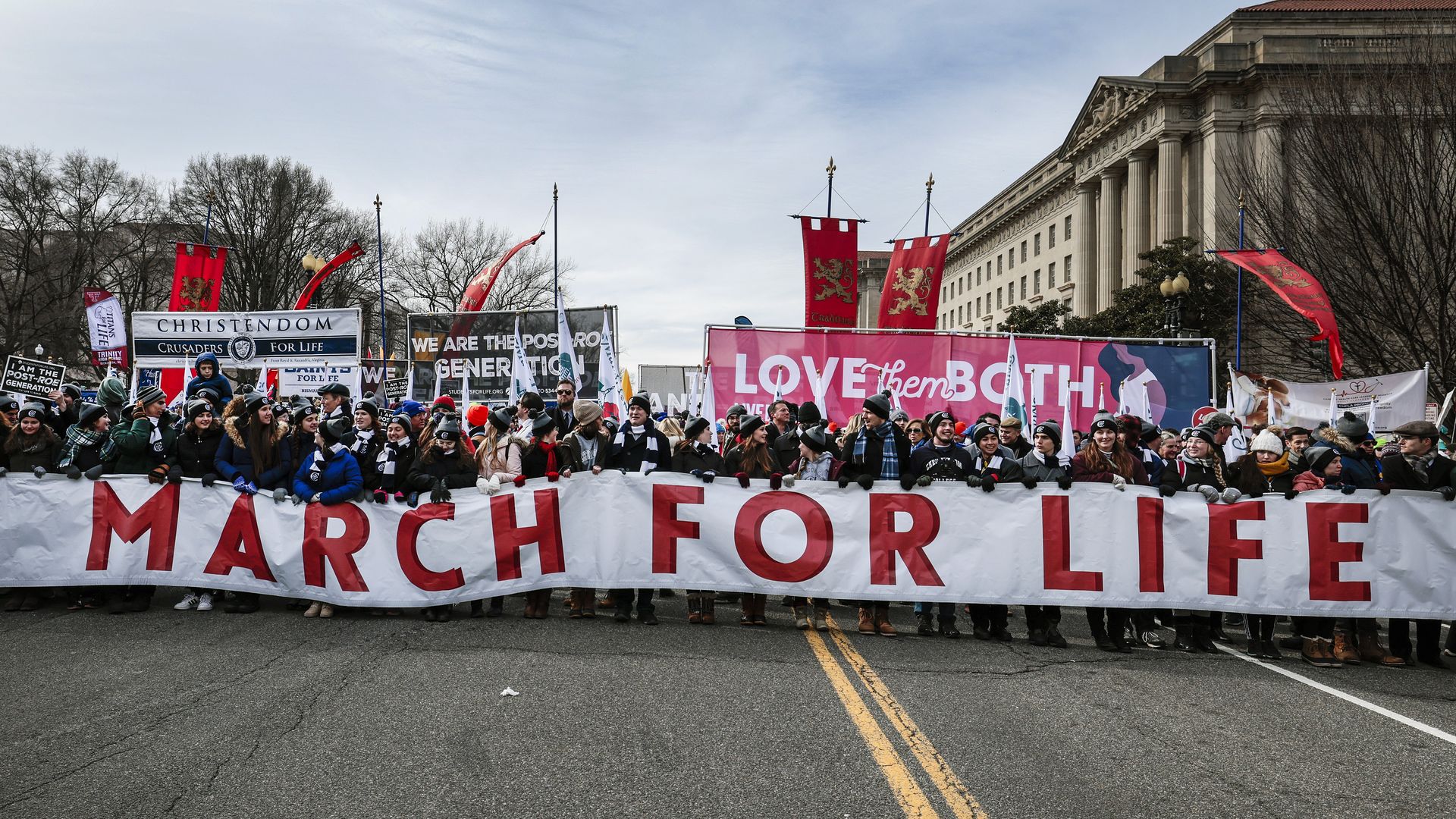 Photo of a crowd of protesters in the streets holding signs, including a long white banner that says "March for Life"