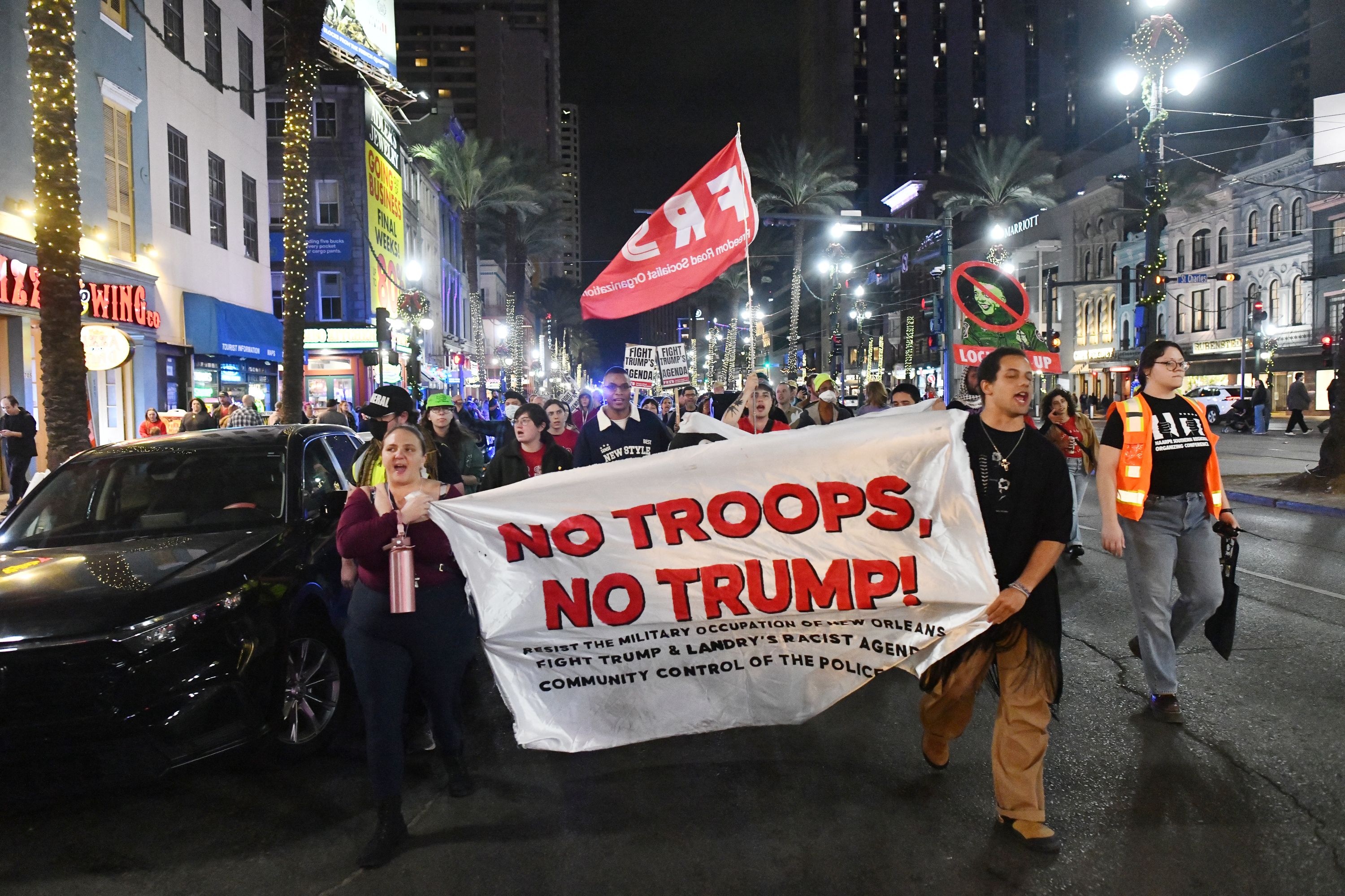 Image shows protesters on Canal Street holding a "NO TROOPS, NO TRUMP" sign.