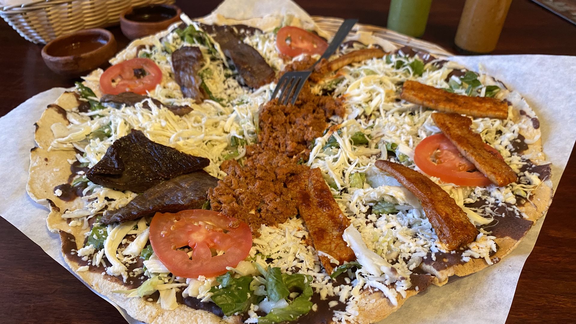 A large crispy tortilla covered in beans, cheese, lettuce, tomatoes and several meats.