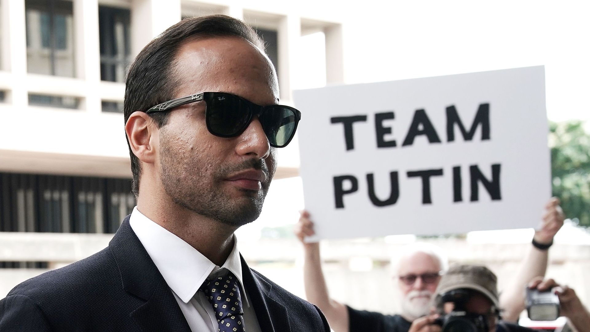 George Papadopoulos walks next to a man with a sign that reads, "Team Putin"