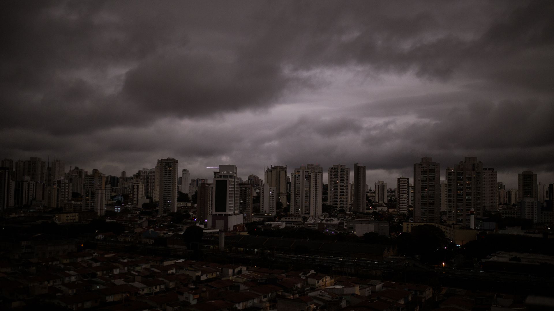 In this image, a darkened and cloudy skyline is seen over a dark city