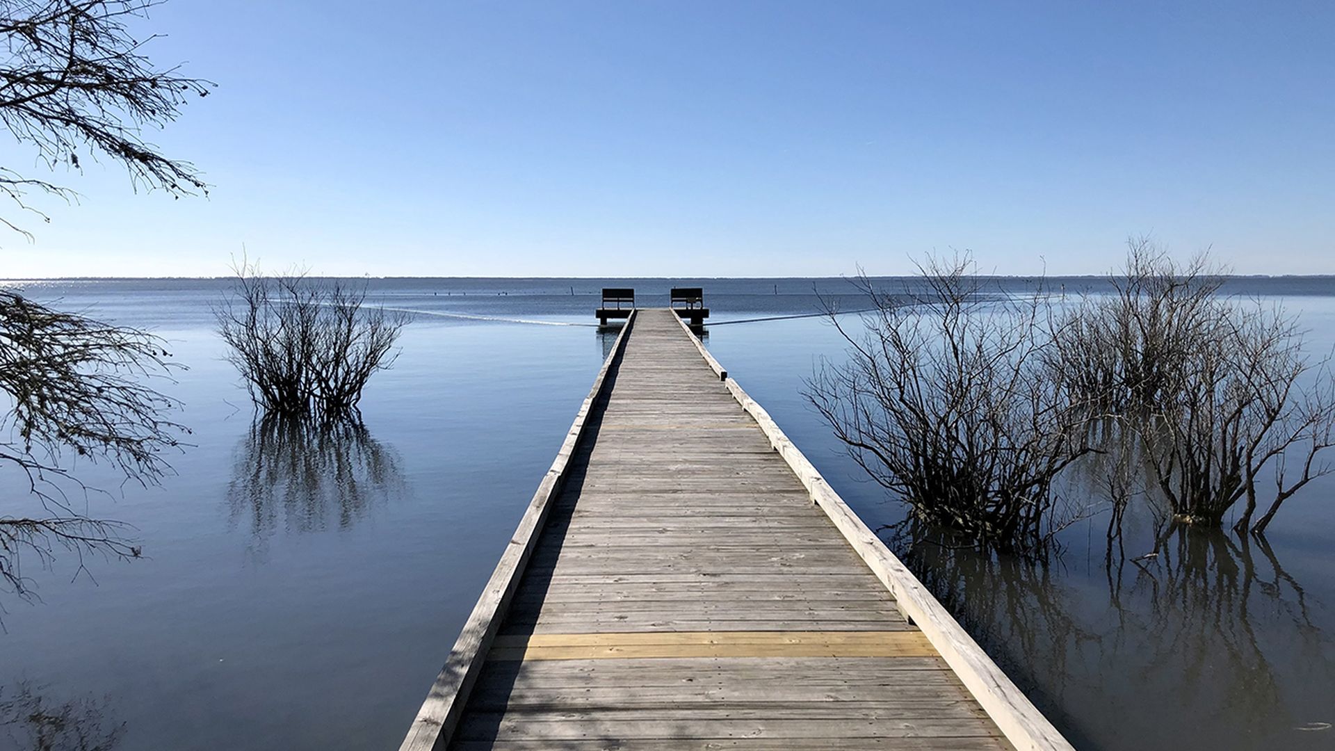 Long wooden boardwalk stretches out over water and overlooks a large blue body of water.