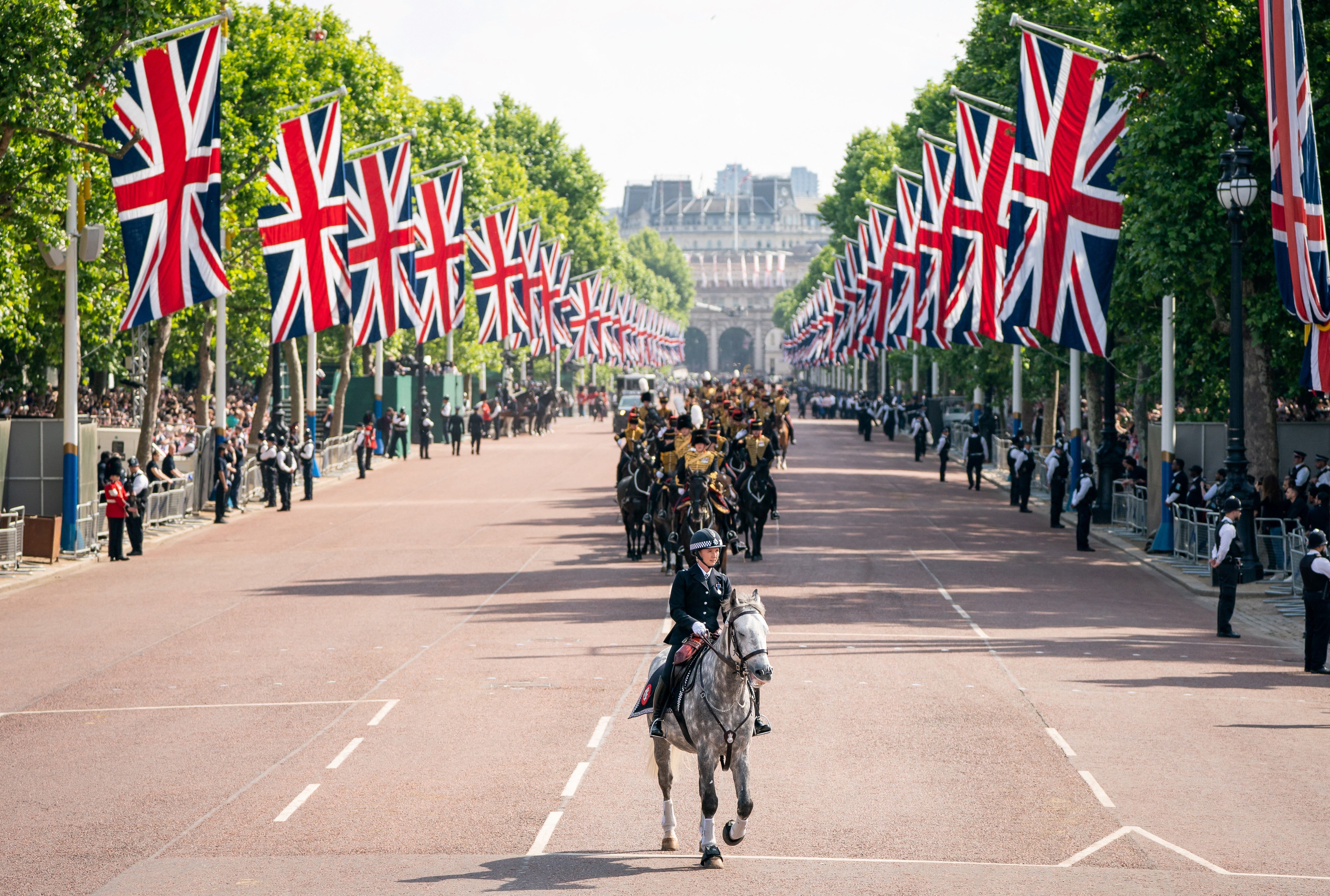 A mounted police officer rides in front of members of the Kings Troop Royal Horse Artillery 