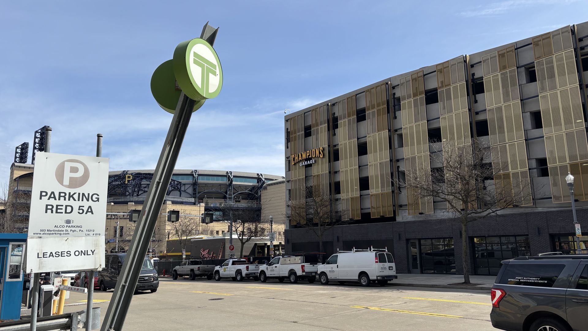 Leaning green circular sign with a white logo above a PARKING RED 5A sign, in front of a building marked CHAMPIONS GARAGE with several white vans parked along the street.
