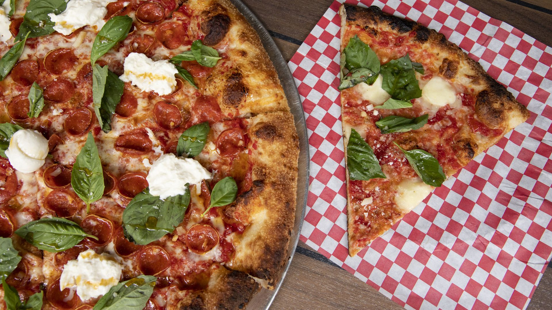 A margherita pizza with a slice next to it on checkered paper