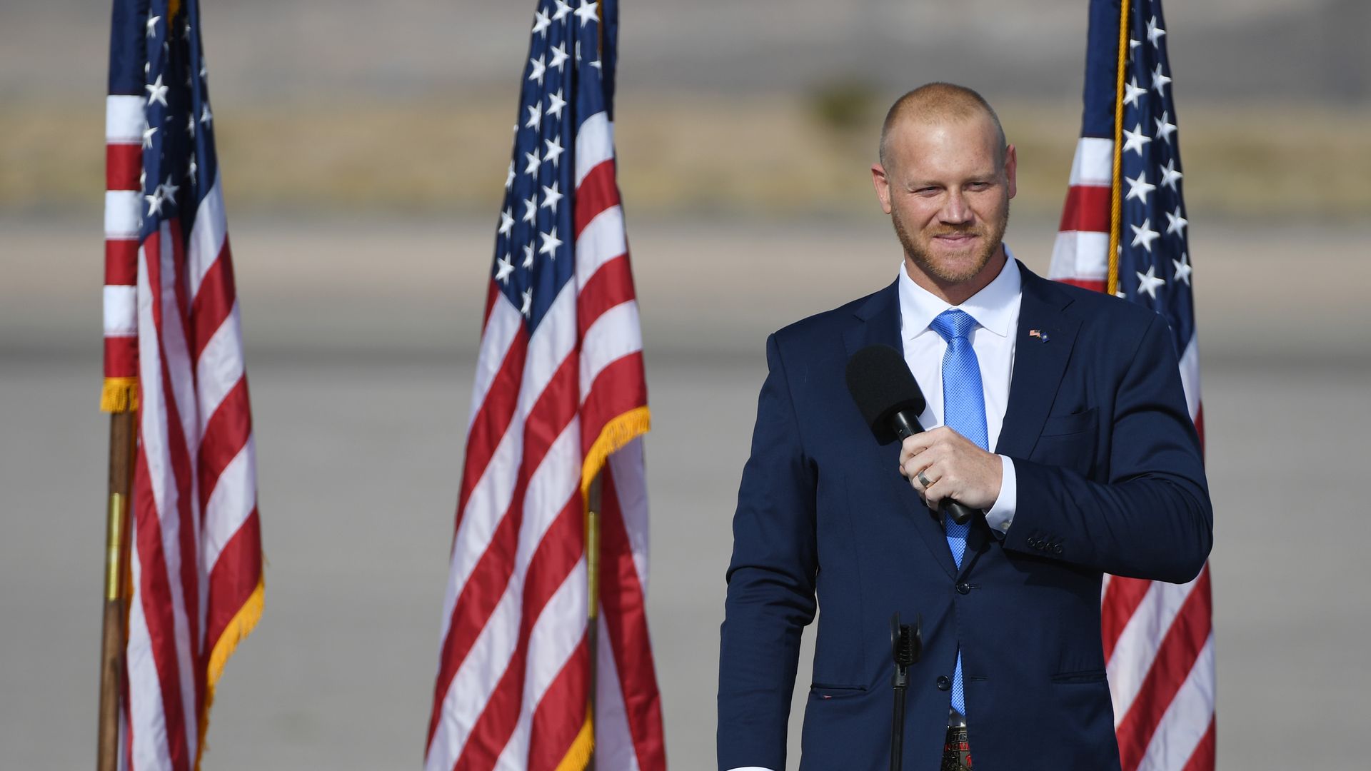 Political candidate and former wrestler Dan Rodimer stands in front of American flags with his left arm bent