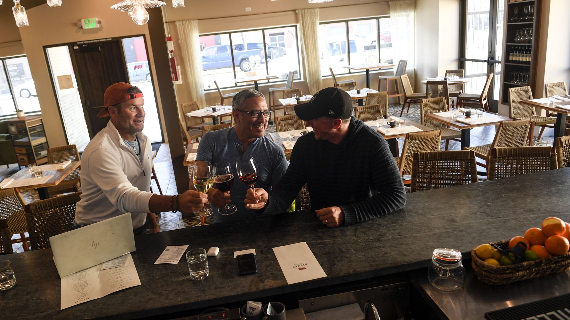 Three men sit at the counter of a bar