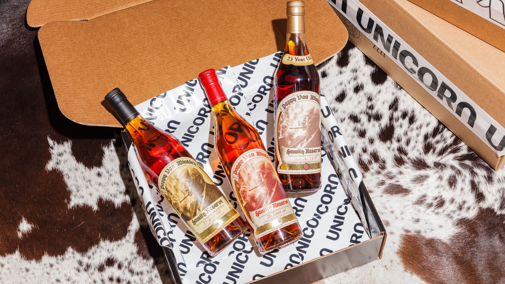 Three bottles of brown liquor in a box with tissue paper with Unicorn in black text.