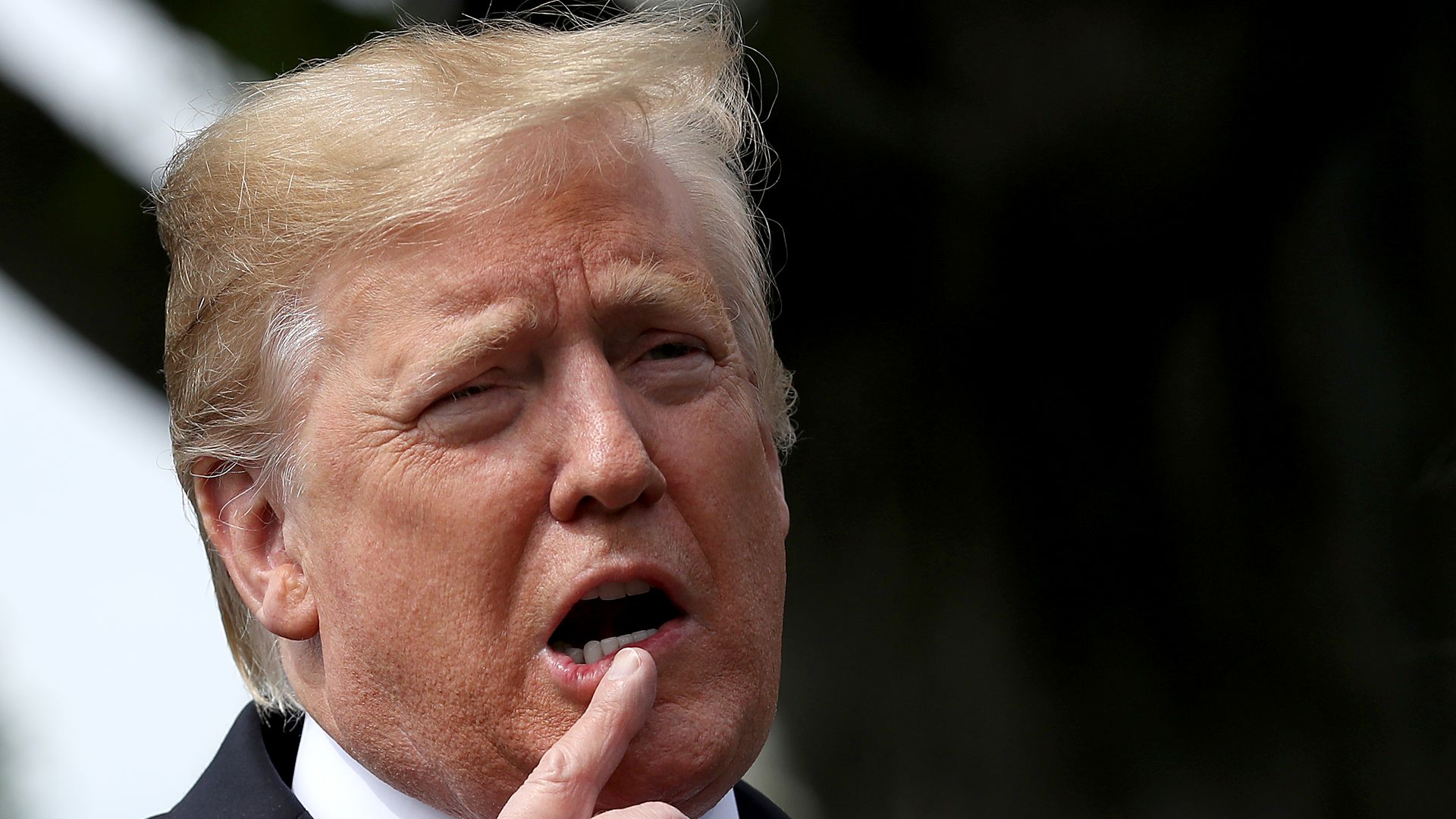 In this image, Trump talks with a hand near his face.