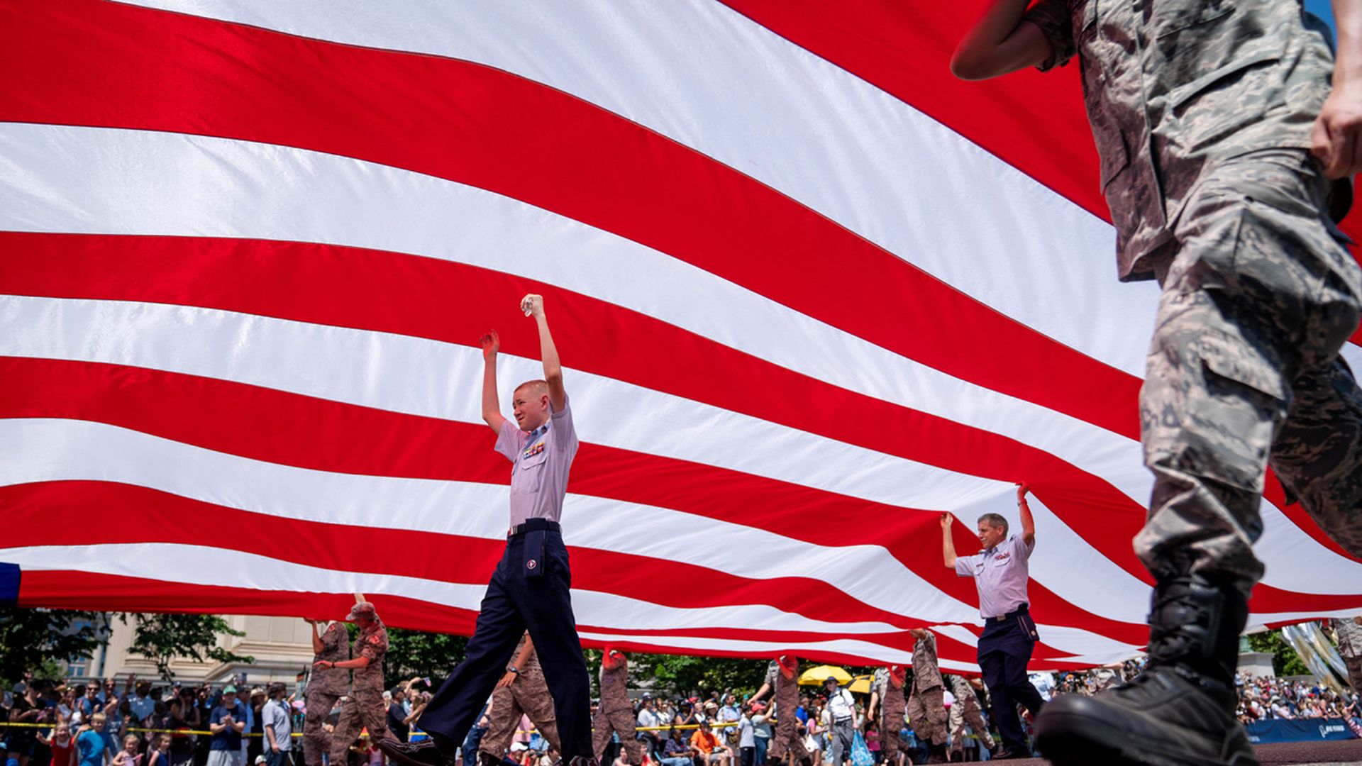 People holding up an American flag as they parade it down a street.