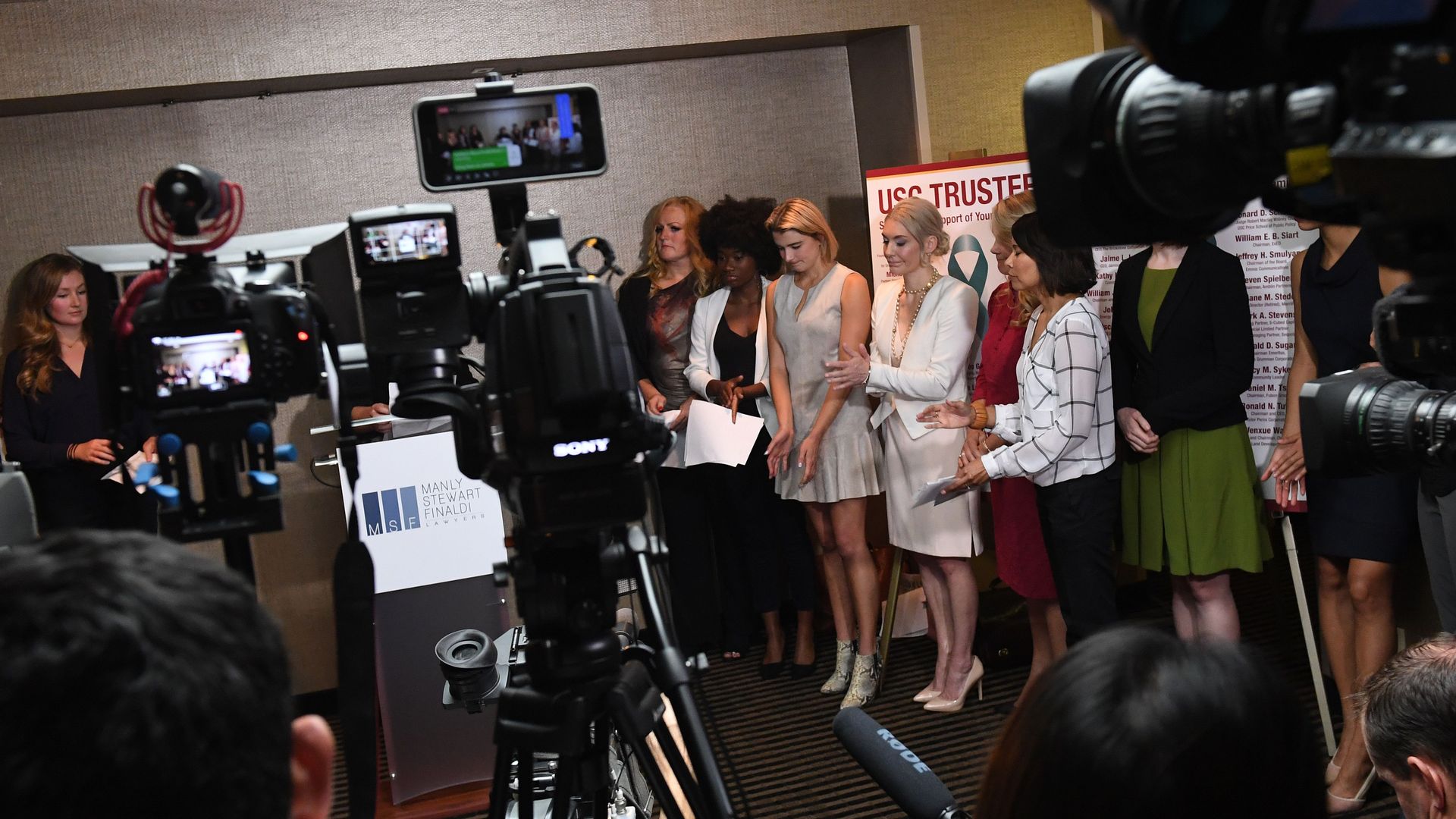 A group of young women stand in front of cameras.