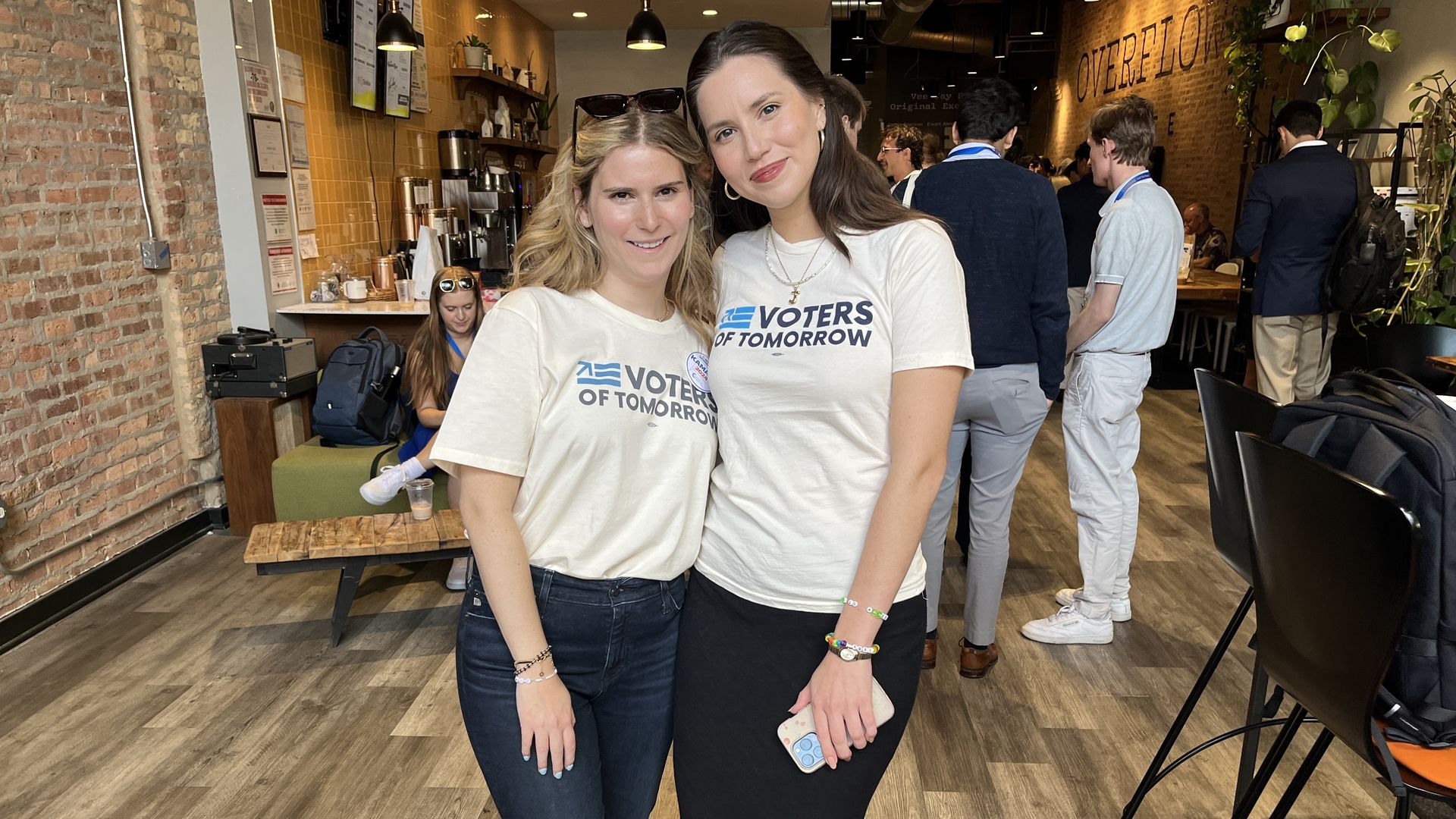 Two people posing in a coffee shop wearing white t-shirts and dark pants.