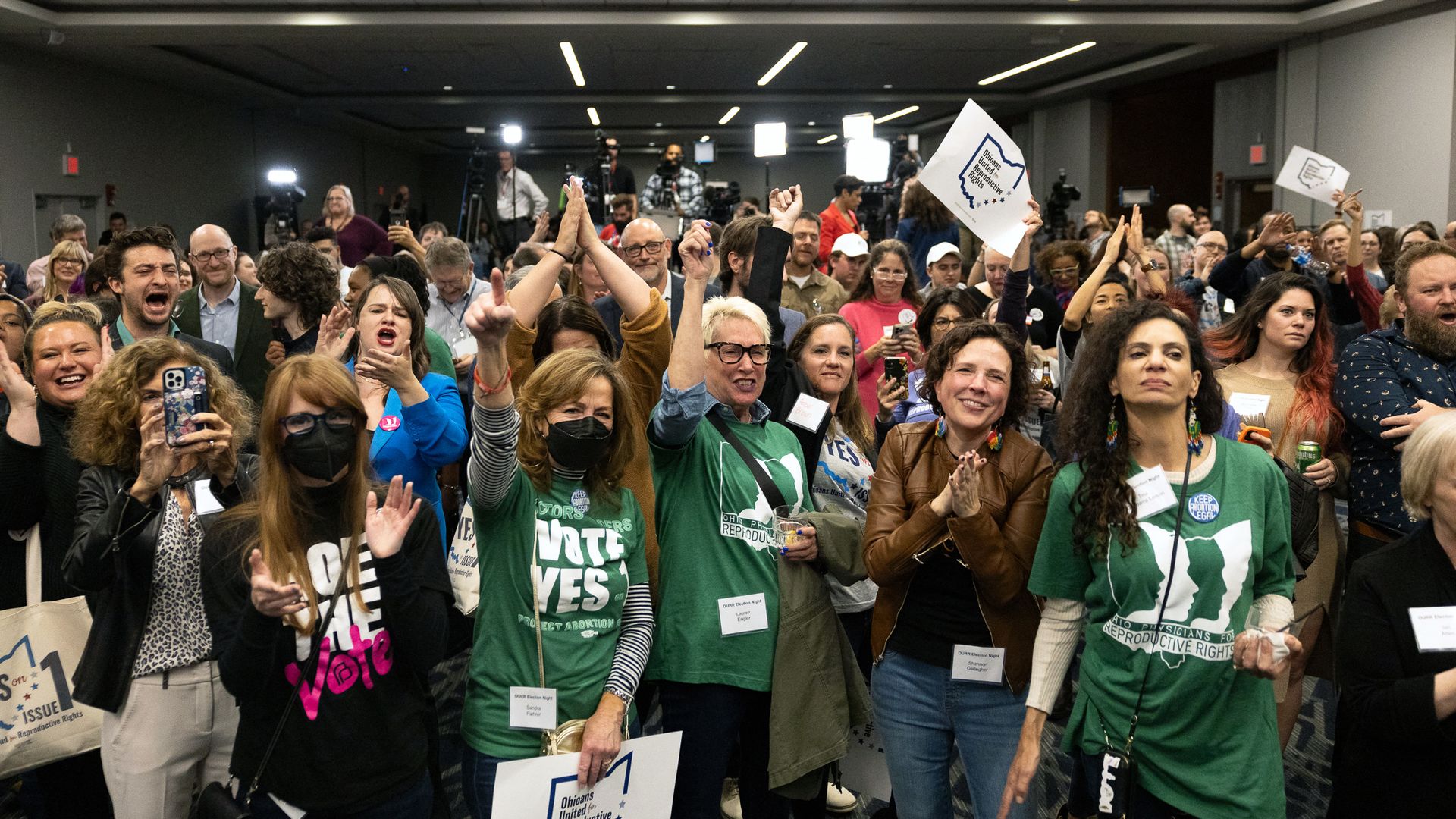 A large group of people cheer and clap, with some holding up signs.