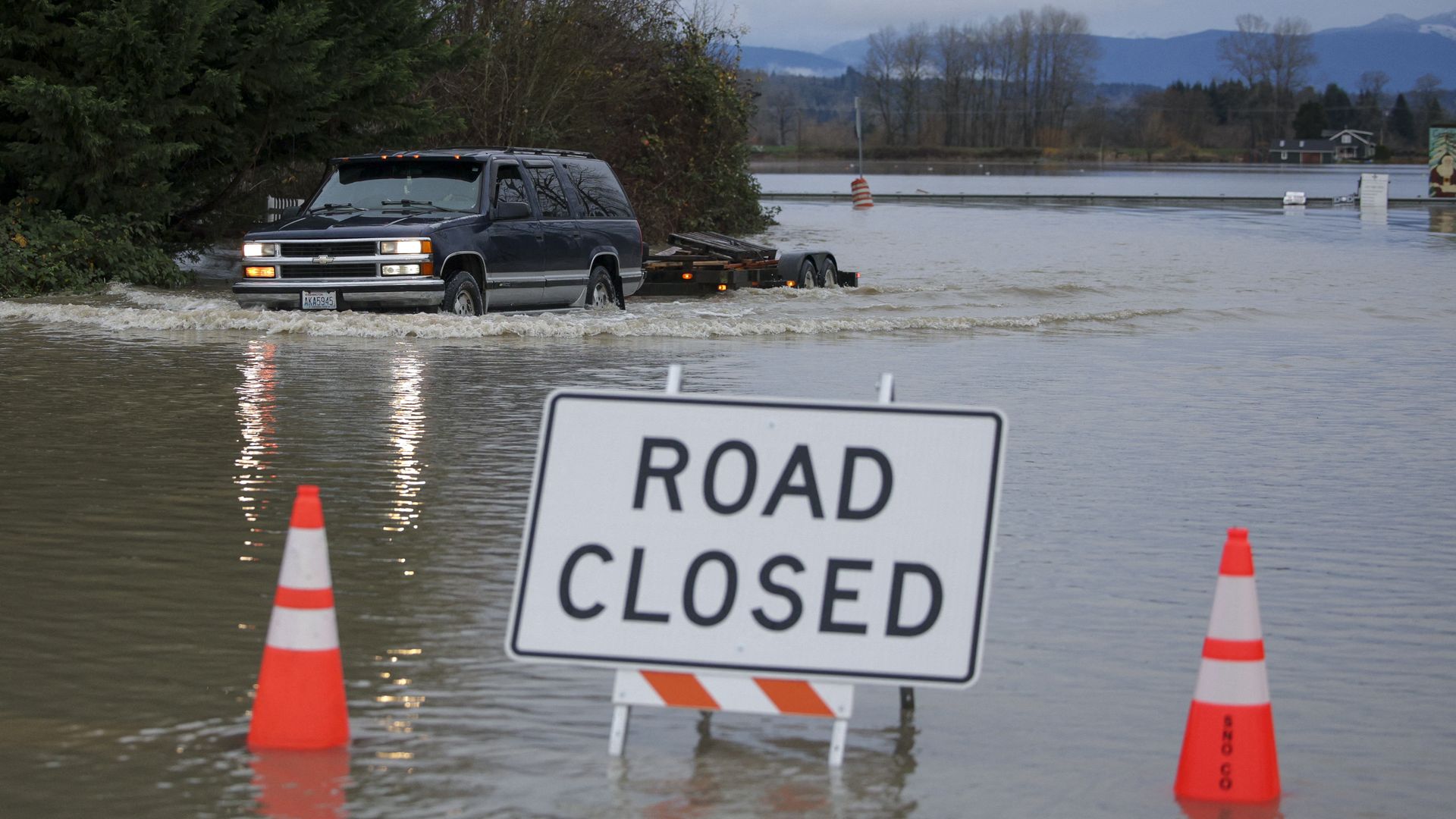 A driver manages to drive through flood waters from the Snohomish River in Snohomish, Washington, near orange and white traffic cones and a sign saying "ROAD CLOSED." (R)