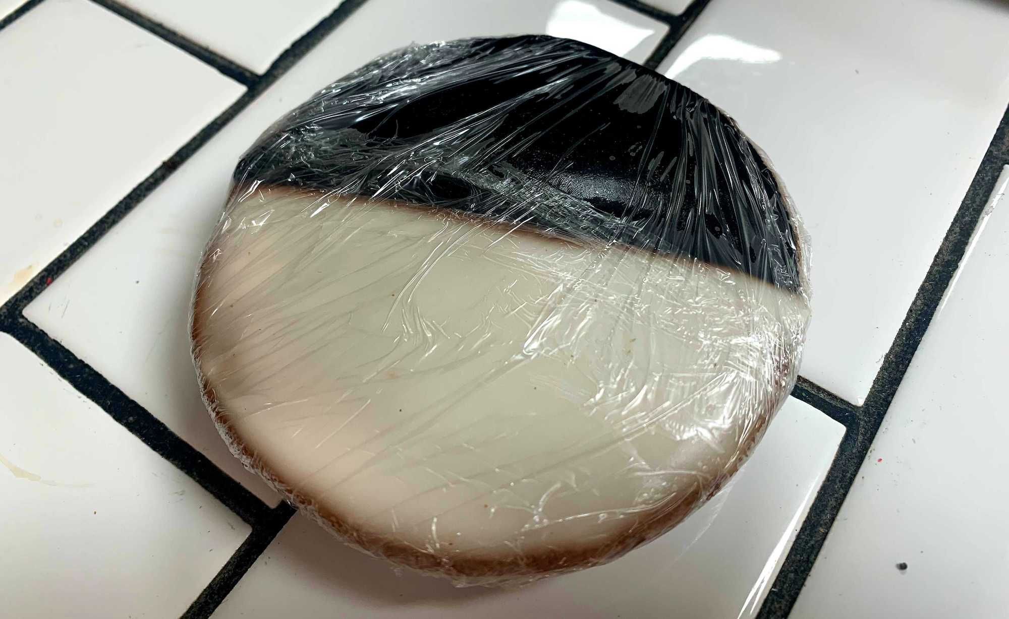 Black and white cookie in saran wrap on tiled counter.
