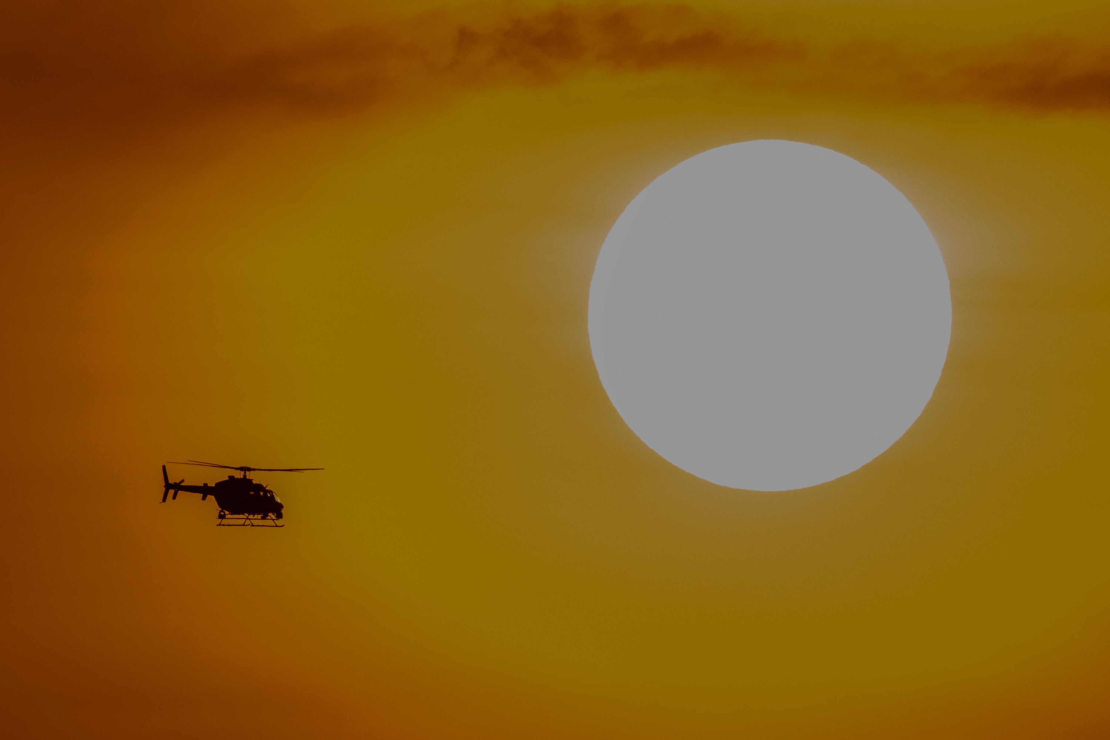 An extremely hazy photograph showing a heliocopter silhouette against a fiery sky. 