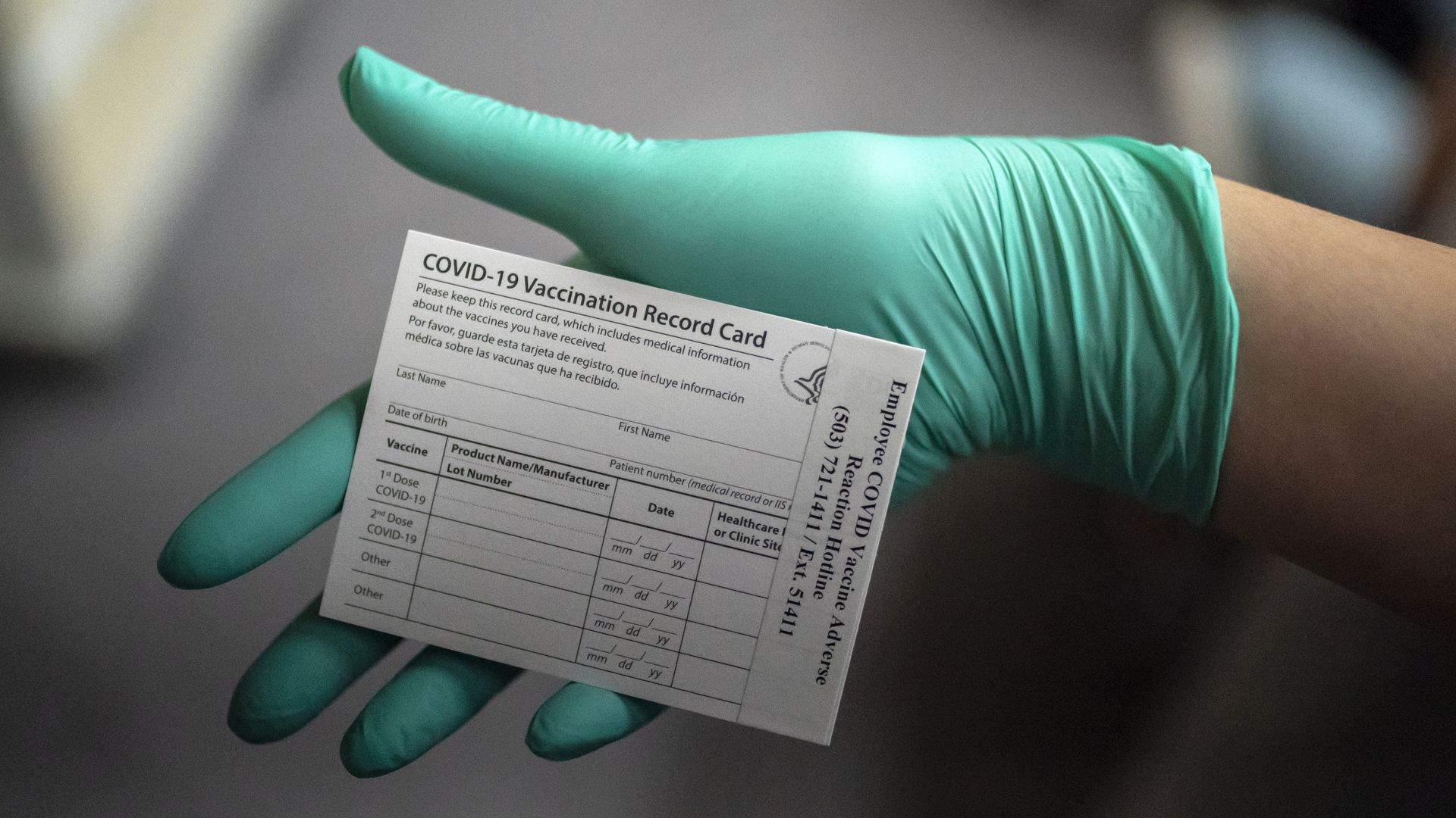 A closeup of a gloved hand holding a blank CDC vaccine card.