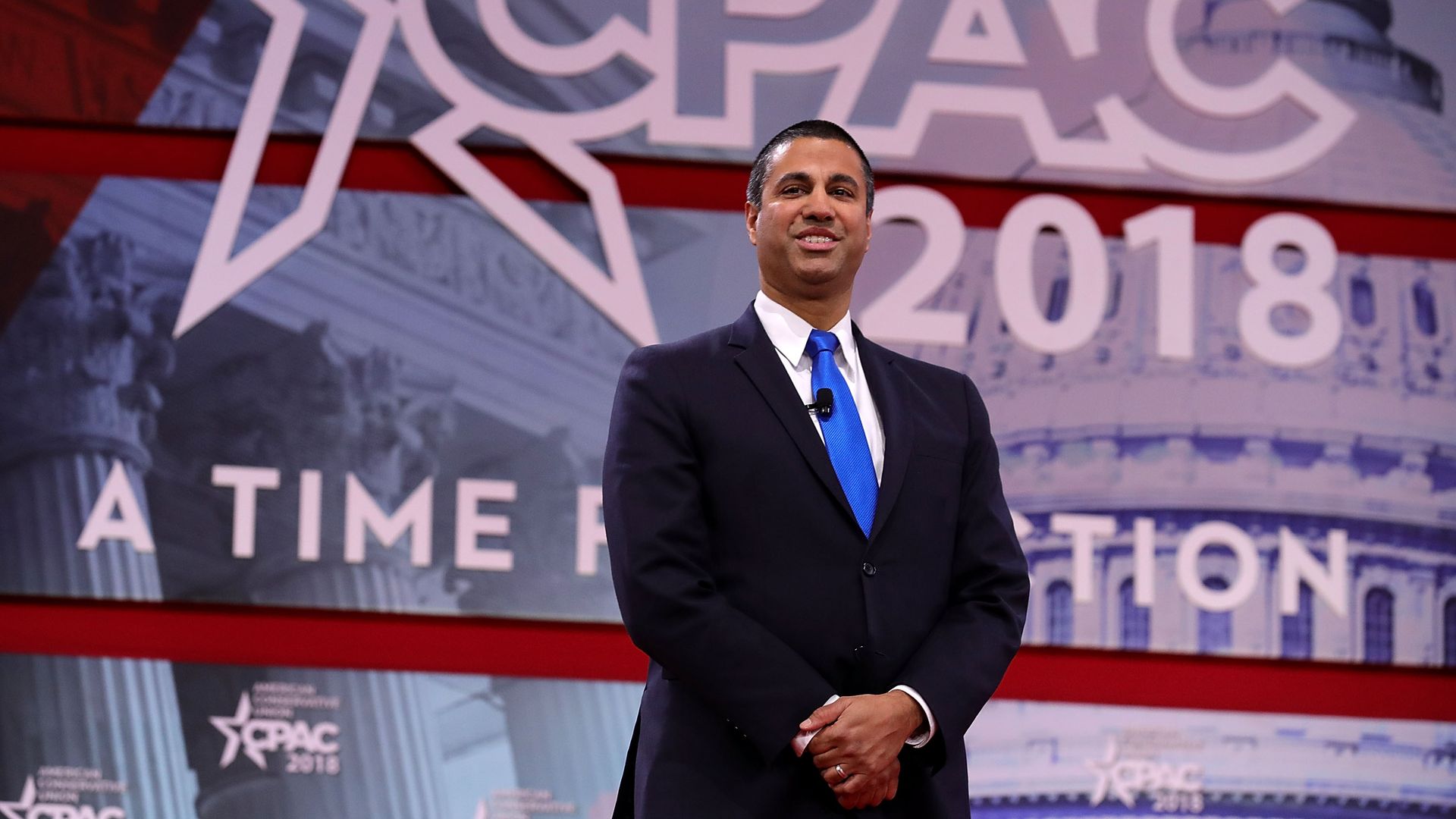 Ajit Pai stands in front of a CPAC sign with his hands clasped